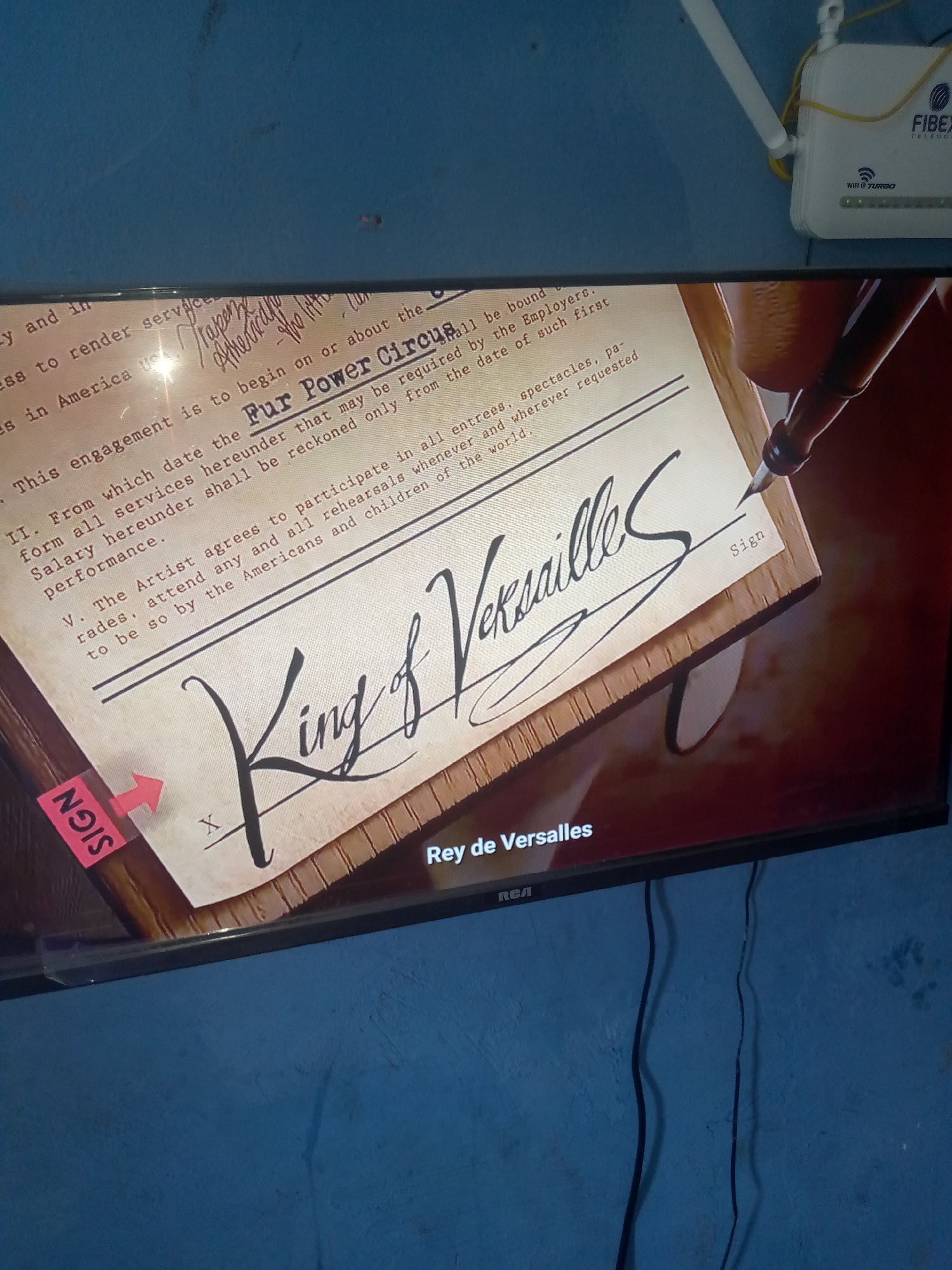 This is a media file, likely a screenshot or a photograph, showing a television screen displaying a scene from what appears to be a historical drama or movie. The on-screen content depicts a close-up of an old document, possibly a contract, with elaborate cursive handwriting.
The document is set on a wooden surface, and a fountain pen is poised as if to sign it. The text on the document refers to an "engagement," "services," "salary," "performances," "rehearsals," and mentions "Fur Power Circus." There is also a prominent signature that reads "King of Versailles." A bright pink sticky note with "SIGN" written on it, and an arrow pointing to the signature line, is attached to the left side of the document. Another smaller "Sign" is visible on the right.
Below the document, on the television screen, text reads "Rey de Versalles" and "RCA," indicating the show title and the TV brand. The background of the television screen is dark and rich, suggesting a dramatic or opulent setting.
In the upper right corner of the image, above the television, a white internet router with antennas is visible, connected by yellow wires. The overall setting appears to be indoors, with a blue, textured wall as the backdrop behind the television. The lighting is dim, with a light source illuminating the document on the screen. The presence of the router suggests a modern-day setting where the media is being viewed, contrasting with the historical content on the screen.