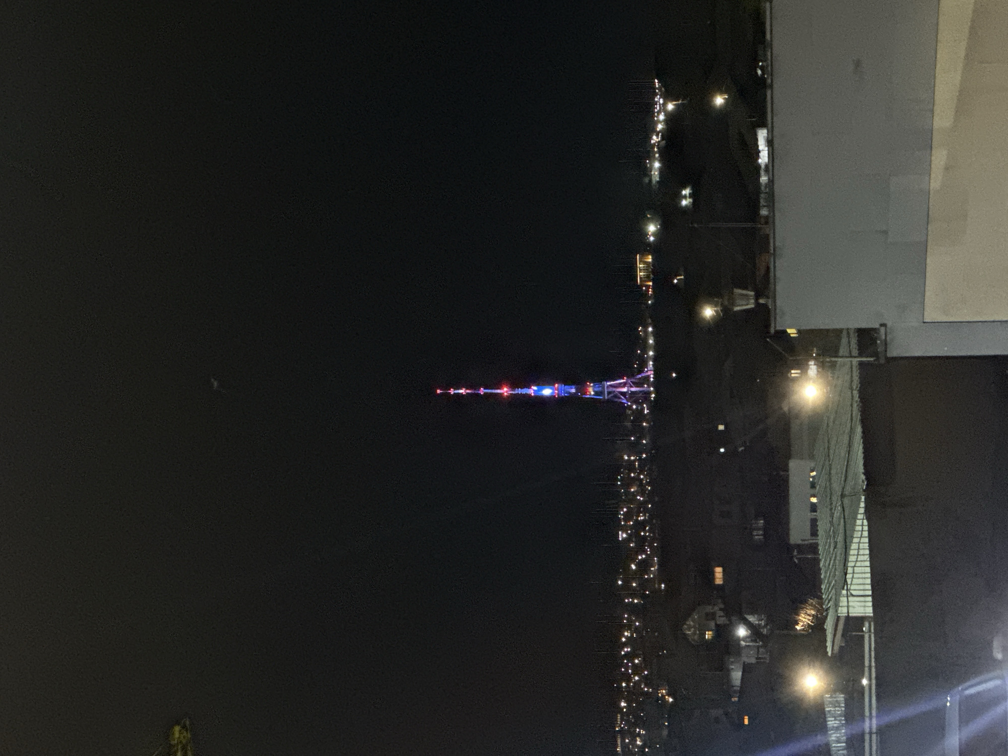The image depicts a night view of Seattle, Washington, featuring the Space Needle illuminated with red, white, and blue lights. A street with streetlights runs along the right of the Space Needle. A building is in the top right corner of the image. The sky is dark.