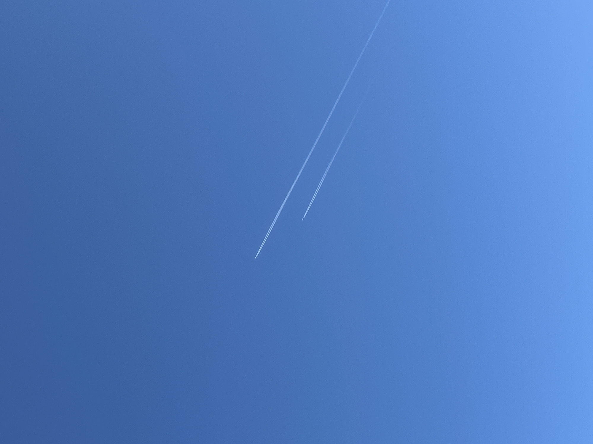 The image shows a bright blue sky with two contrails from aircraft. There is no information in the image to indicate this is in the city of Chaikovsky, Russia.