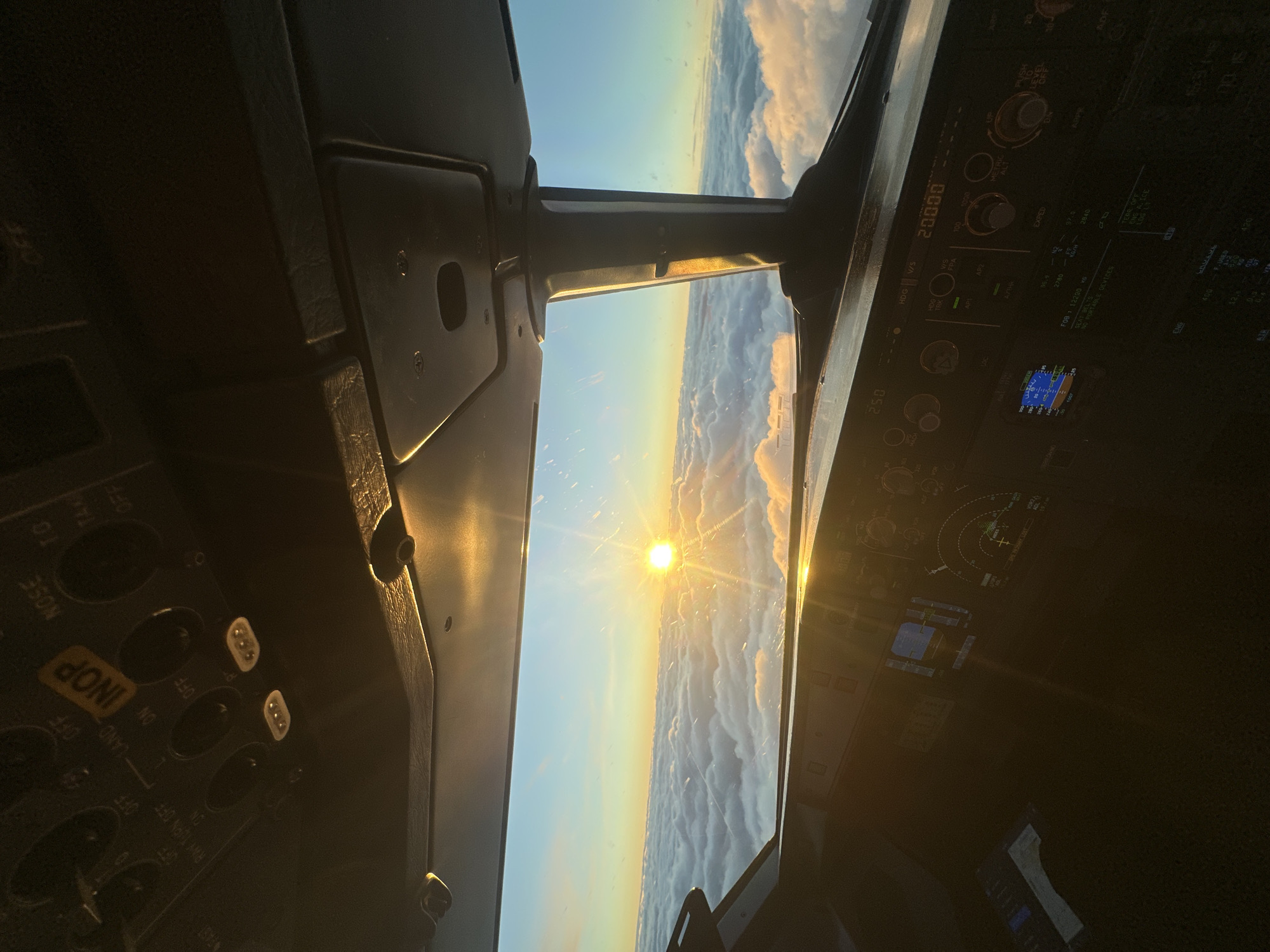 The image shows a view from inside the cockpit of an aircraft. The sun is visible through the windshield, shining brightly above a layer of clouds. The cockpit's control panel is visible, with various switches, dials, and displays. The altitude is displayed as 20000. The aircraft is flying over a blanket of clouds at sunrise or sunset. The city of Khimki, Russia is not visible in this image.