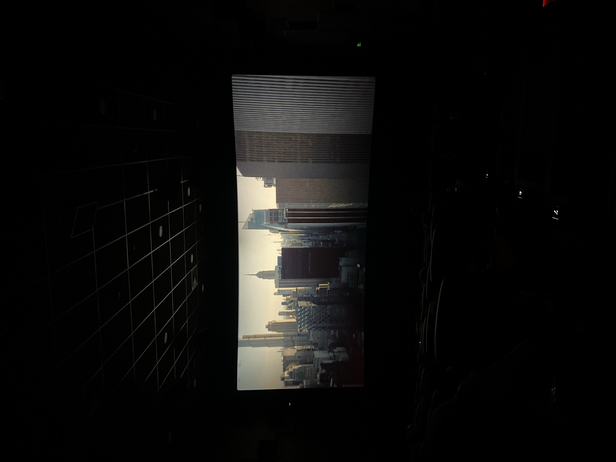 The image shows a movie screen in a dark room, likely a cinema. The screen displays a cityscape with tall buildings. The twin towers of the World Trade Center are visible, as well as the Empire State Building. The perspective suggests the photo was taken in the United States, not in Yerevan, Armenia. Other details, like chairs or people, are not clearly visible in the dark environment.