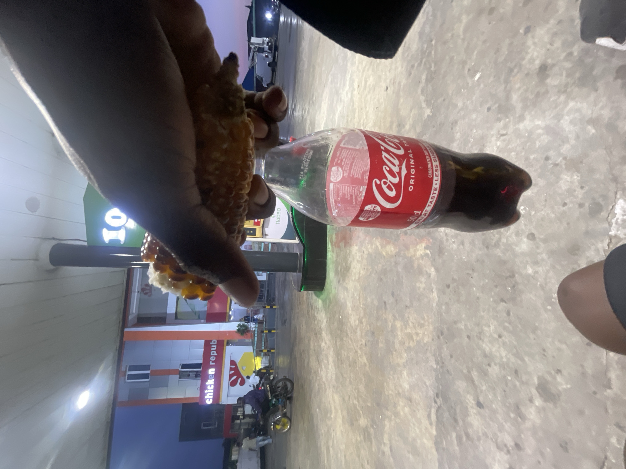 A person holds fried food and a Coca-Cola bottle near a Chicken Republic restaurant in Lokoja, Nigeria.