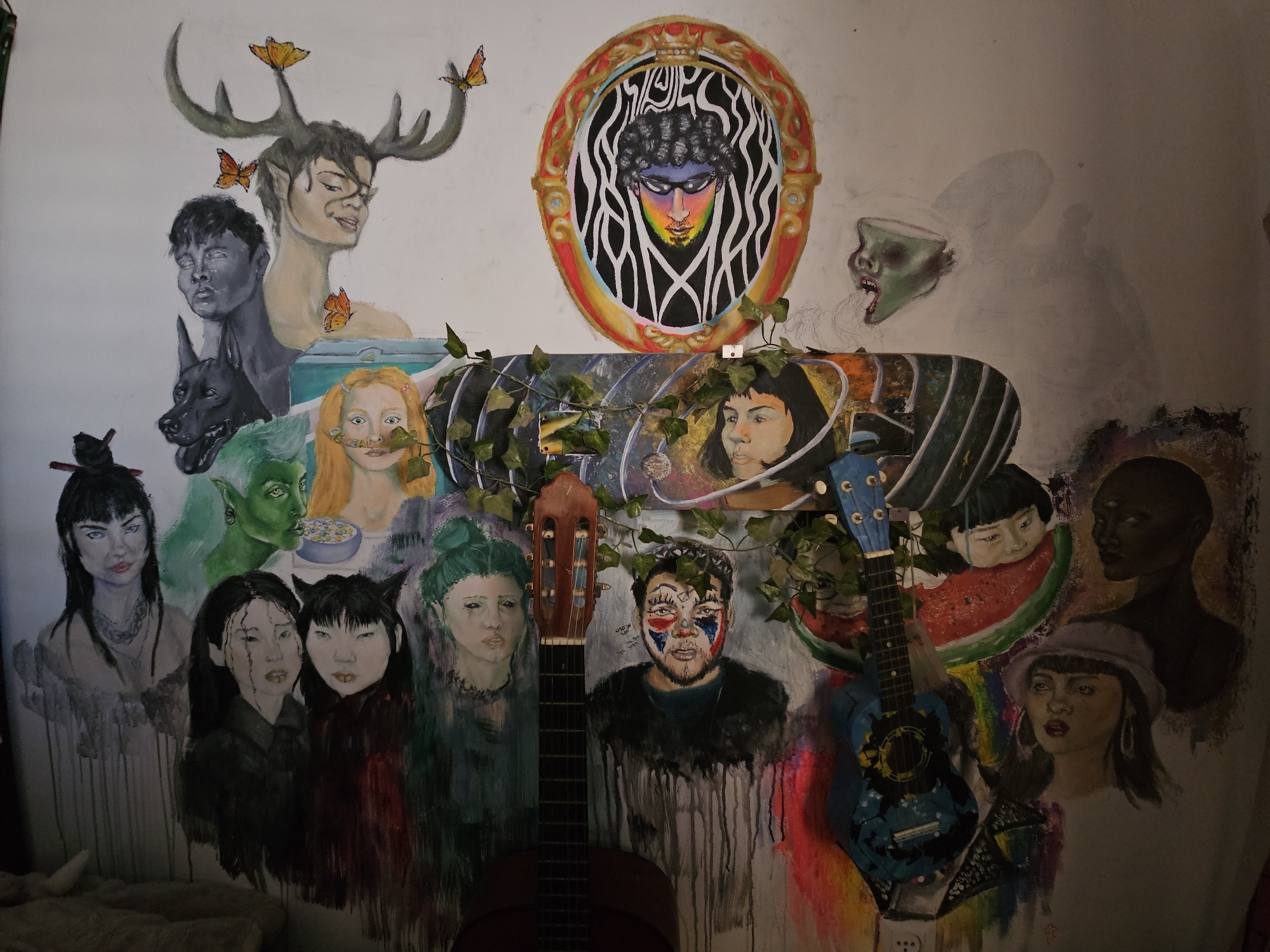 This image depicts a colorful and eclectic mural painted on a wall in Rishon LeZion, Israel. The mural features a variety of figures, including humans with unique features, animals, and fantastical creatures.
In the upper section of the mural, a figure with antlers and butterflies is depicted. To its left, a dark-skinned figure with a somber expression is shown, alongside a black dog. Further to the right, a stylized portrait in an oval frame showcases a person with curly hair and vibrant, rainbow-colored face paint, surrounded by abstract black and white lines. Adjacent to this, a grotesque, green-skinned head with an open mouth is painted, appearing to emerge from the wall.
The central part of the mural is dominated by a horizontal element, possibly a painted skateboard or a similar object, adorned with greenery and images. On this element, several faces are painted: a woman with red hair and a quizzical expression, a woman with dark hair and a pensive look, and a child's face peering from behind a slice of watermelon. To the right, a dark-skinned figure with three eyes is depicted.
The lower section of the mural presents more faces. On the left, a woman with dark hair and dramatic makeup is featured. Next to her, two women with dark hair are painted closely together. Further right, a woman with green hair and a serene expression is shown. In the center foreground, a man with clown-like face paint is depicted, with text in Hebrew above him. To the right of this figure, a woman with a hat and hoop earrings is painted.
Two guitars are positioned in front of the mural, one in the center foreground, a classical guitar, and another, a blue ukulele-style guitar, to the lower right. The guitars partially obscure the painted figures behind them. The overall impression is one of artistic expression and perhaps a shrine or creative space within a home or studio. The lighting suggests an indoor setting, with shadows cast on the wall.