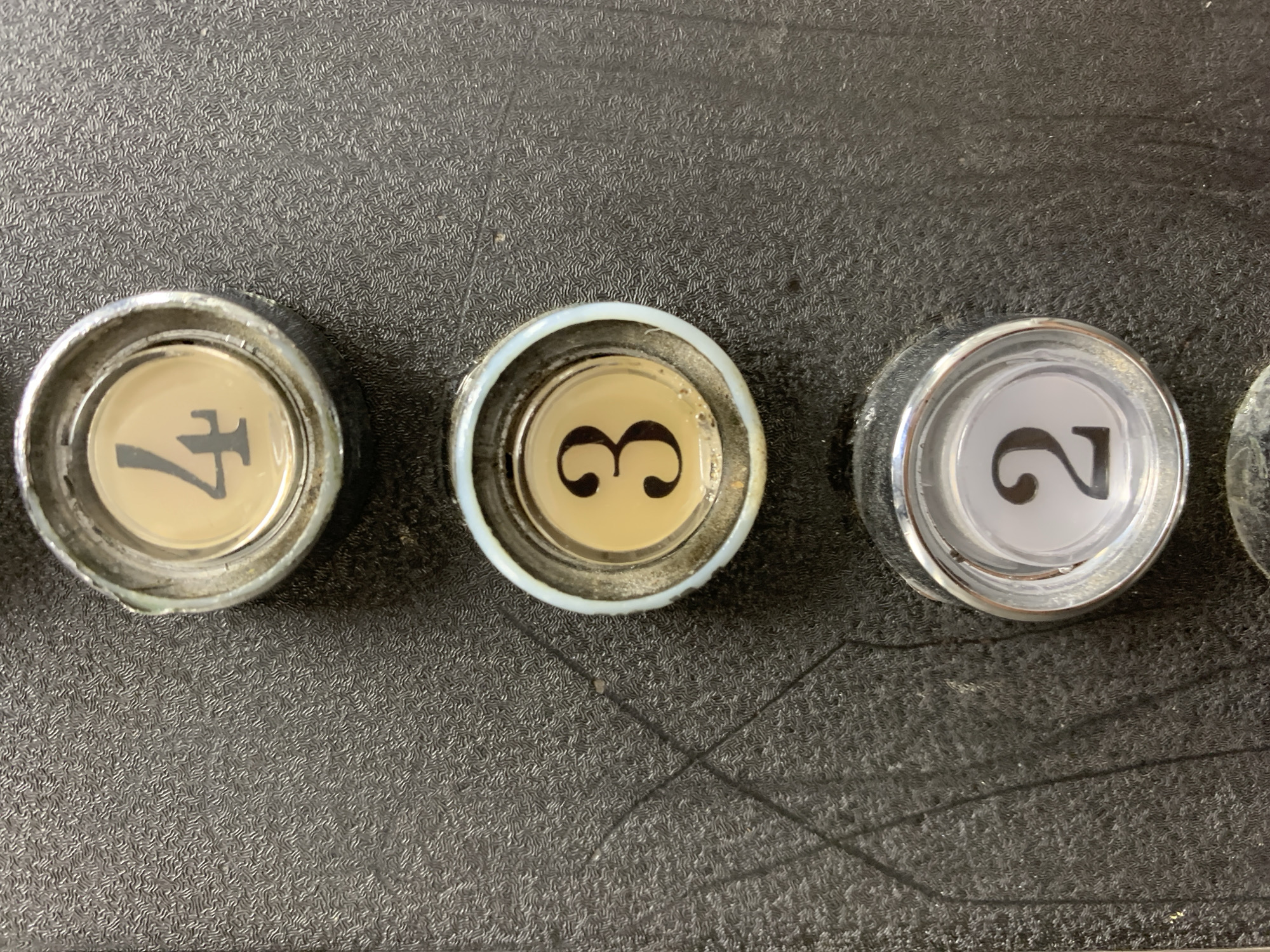 The image displays a close-up, straight-on view of three elevator buttons on a textured, dark gray panel. The buttons are arranged vertically and are numbered 4, 3, and 2 from top to bottom. Each button has a metallic surround and a circular inset displaying the number. The number 4 is a light tan color with a black numeral. The number 3 is also light tan with a black numeral. The number 2 is white with a black numeral. The panel shows some surface wear and appears to be inside a building. There is no information in the image to suggest a specific location in Barcelona, Spain.