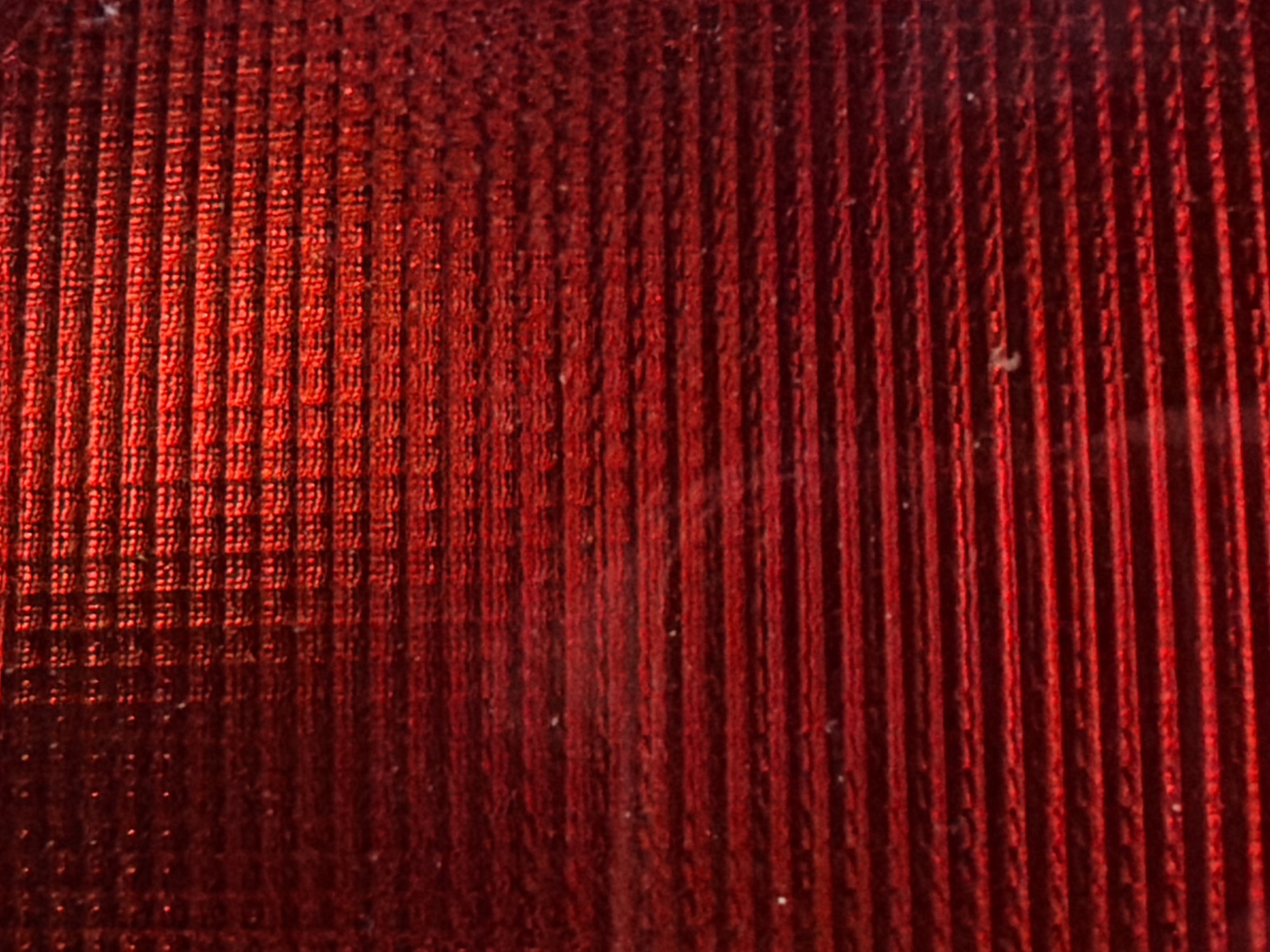 The image shows a close-up of a red textured surface, possibly a fabric or a material with a ribbed pattern. The lighting creates strong highlights and shadows, emphasizing the texture. There are no people, identifiable objects, or environmental context visible that would allow for localization in Nha Trang Ward, Vietnam. The image is purely an abstract representation of a material's surface.