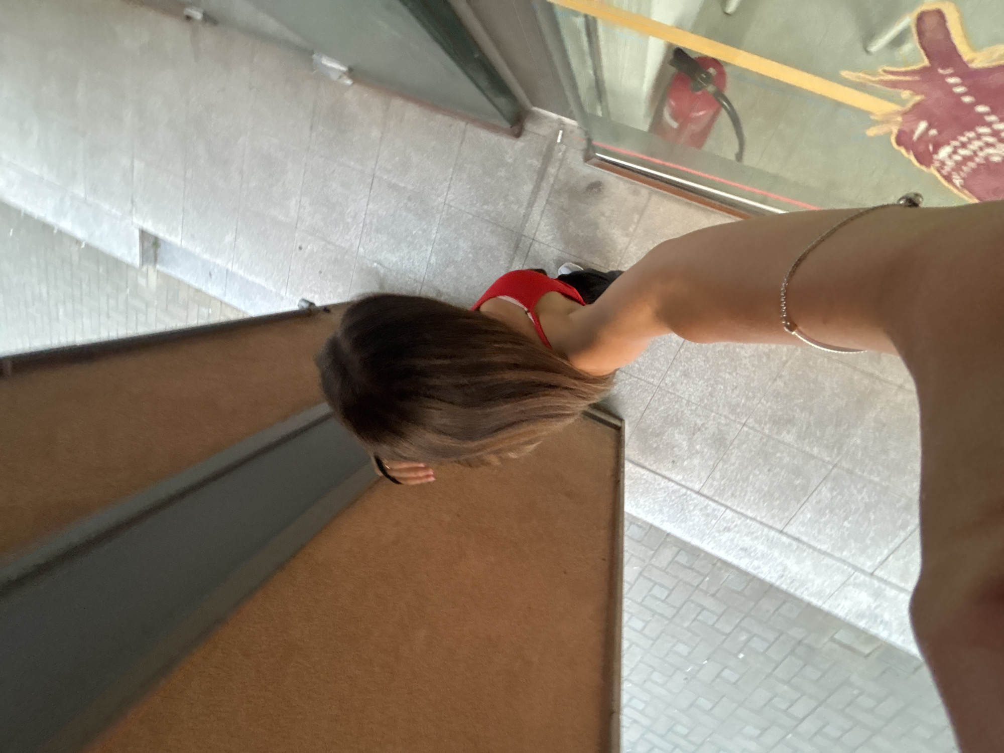 A high-angle shot of a person with brown hair wearing a red top, standing on a tiled surface. The person is near a wooden structure and what appears to be a window or glass panel with a reflection. The exact location within Sofia, Bulgaria, cannot be determined with the given information.