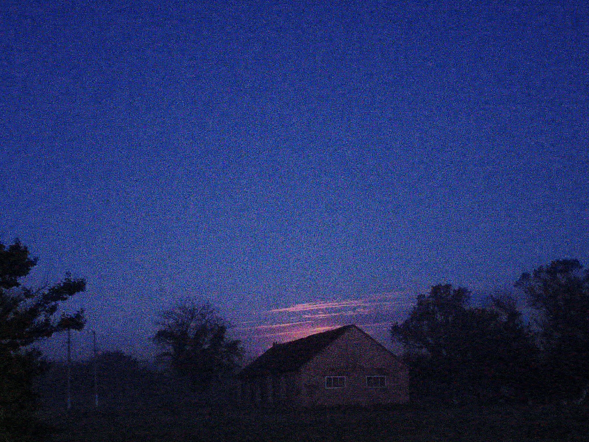 A photograph shows a building at dusk in a rural environment. The sky is a dark blue, and there are some pink clouds near the horizon. A dark building is in the foreground, obscured by foliage. Due to the limited detail, it's difficult to provide a specific location within Ustyvytsia, Ukraine, or other details.