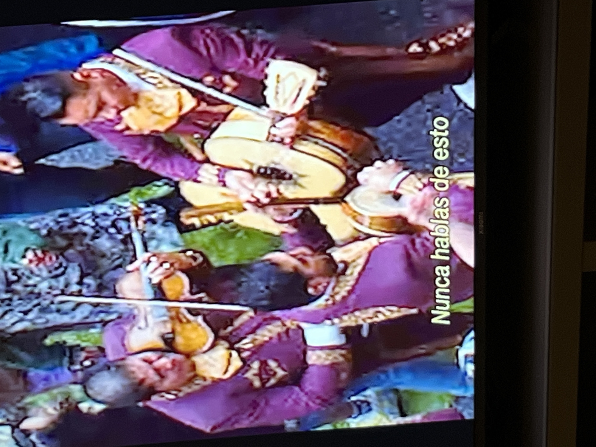 The image shows a mariachi band performing. The musicians are wearing traditional purple mariachi suits with gold trim. They are playing violins and guitars. The text "Nunca hablas de esto" is visible on the right side of the image. Based on the attire and instruments, they are playing traditional Mexican music. The location cannot be determined from the image.