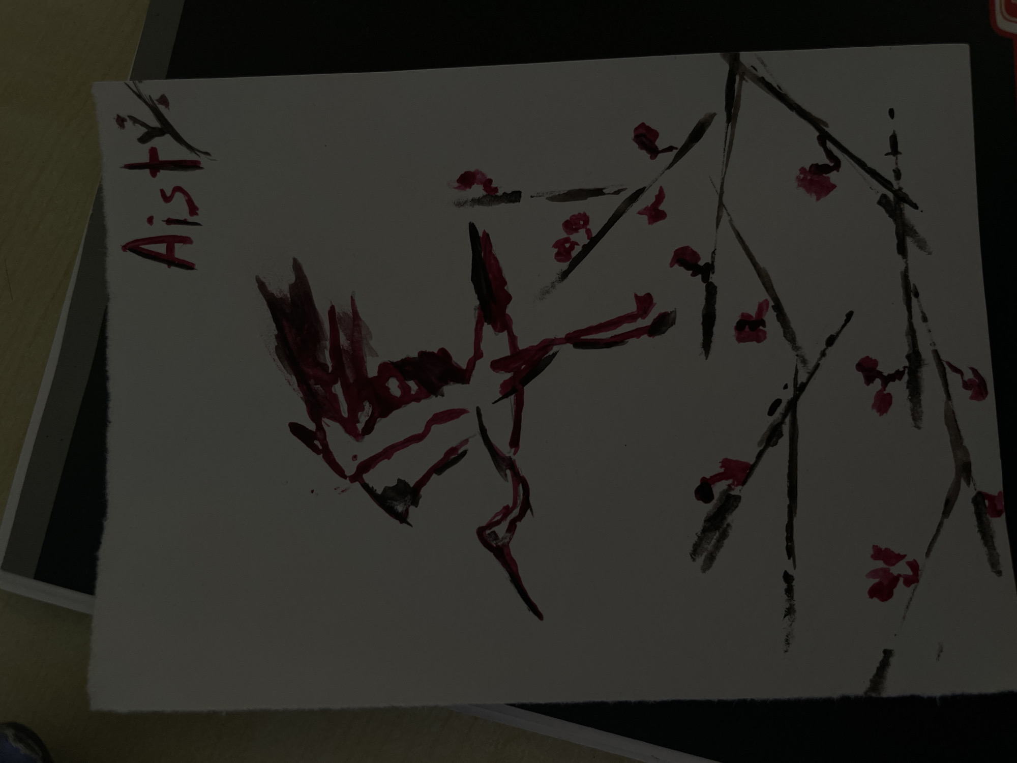 The image shows a watercolor painting of a red-crowned crane flying among branches with pink blossoms. The painting is on white paper with a torn edge. The word "Aisty" is written in red and black ink in the top right corner. The painting is set against a dark background, possibly a table. No specific location in Minsk, Belarus, is depicted.
