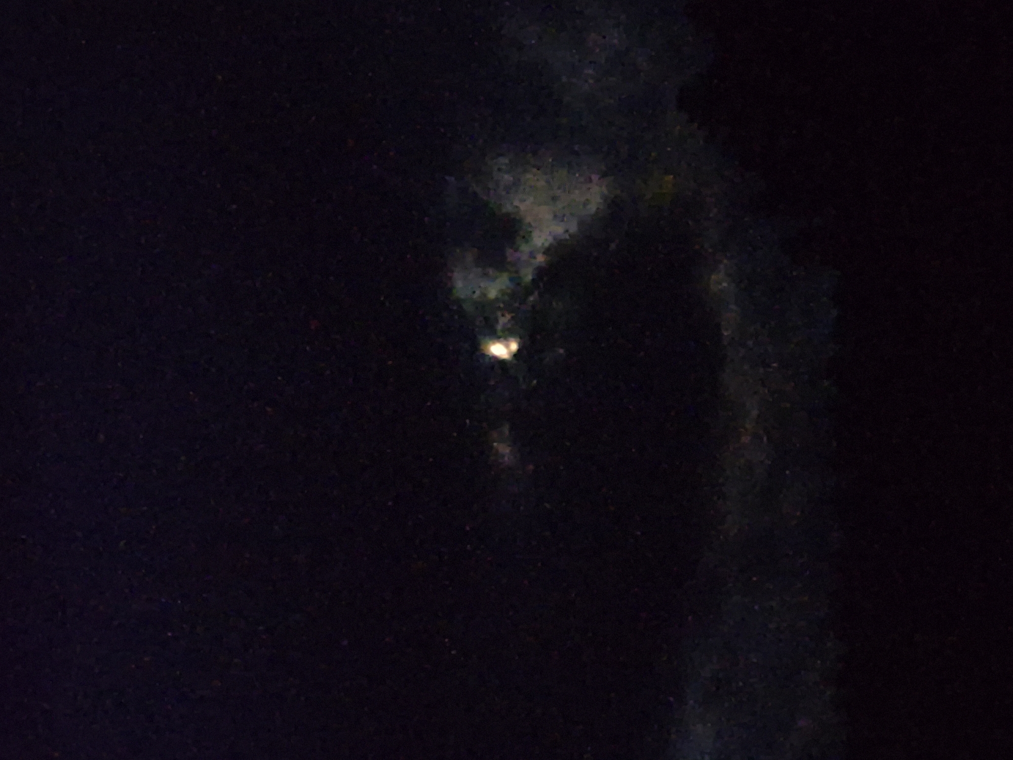 The image depicts a nighttime scene with a dark sky filled with scattered, faint specks of light, suggesting stars or distant lights. A faint, hazy glow is visible in the center, partially obscured by darker clouds or atmospheric conditions. The lower portion of the image shows a dark, indistinct silhouette of what appears to be trees or a landscape, suggesting an outdoor setting. There are no discernible people, specific objects, or actions in the image. The location in Sooblase, Estonia cannot be determined from the visual information provided.