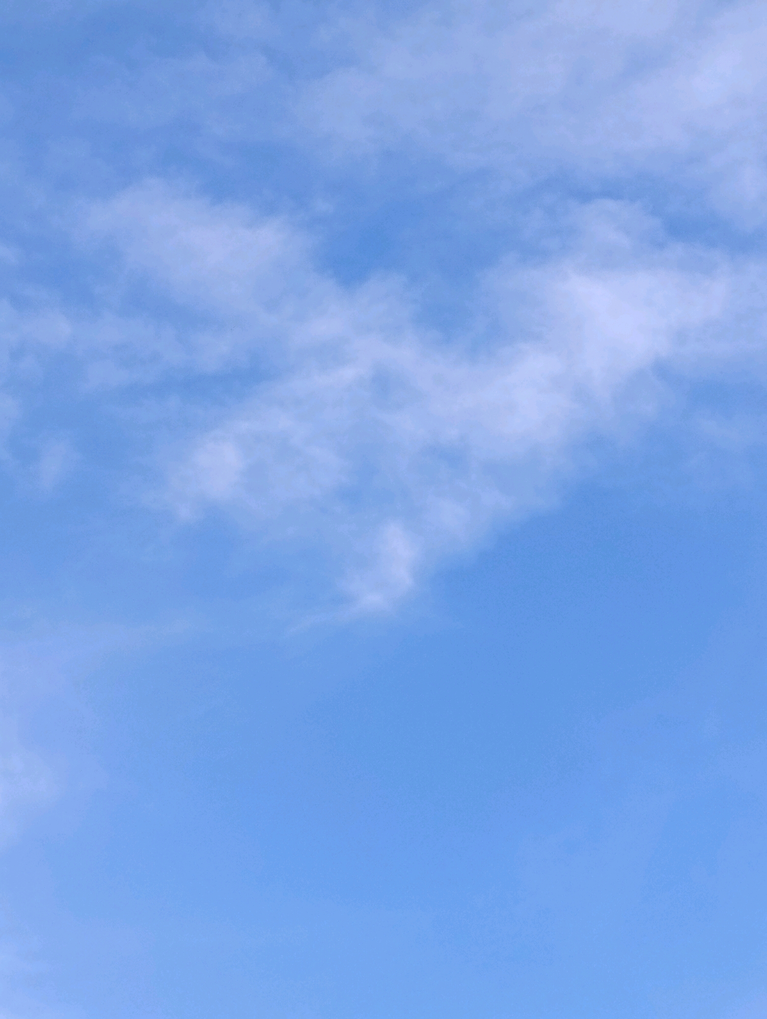 The image is a photograph of a clear blue sky with scattered wispy white clouds. The clouds are thin and feathery, suggesting fair weather. The lighting indicates it is daytime, likely mid-morning or afternoon. The image does not contain any identifiable landmarks or features that would allow for pinpointing a specific location within Setúbal, Portugal. It is a generic view of the sky.
