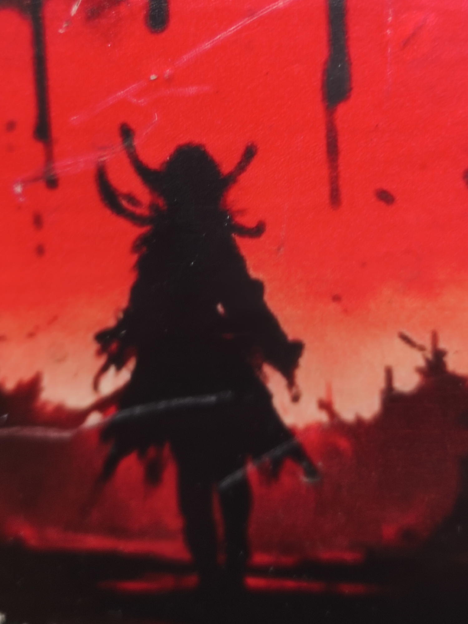 The image shows a silhouette of a figure with elaborate horns or a headdress against a vibrant red background. The figure appears to be standing, with a dark, flowing garment. Its arms are outstretched or positioned in a way that suggests movement or action. The background is a rich, almost luminous red, with some darker, abstract splatters or drips that could be interpreted as ink or paint. There are also hints of a dark, abstract landscape or ground beneath the figure. The overall impression is dramatic and somewhat menacing, with the stark contrast between the black silhouette and the intense red. The red could evoke a sense of urgency, passion, or even danger. There is no discernible text in the image.