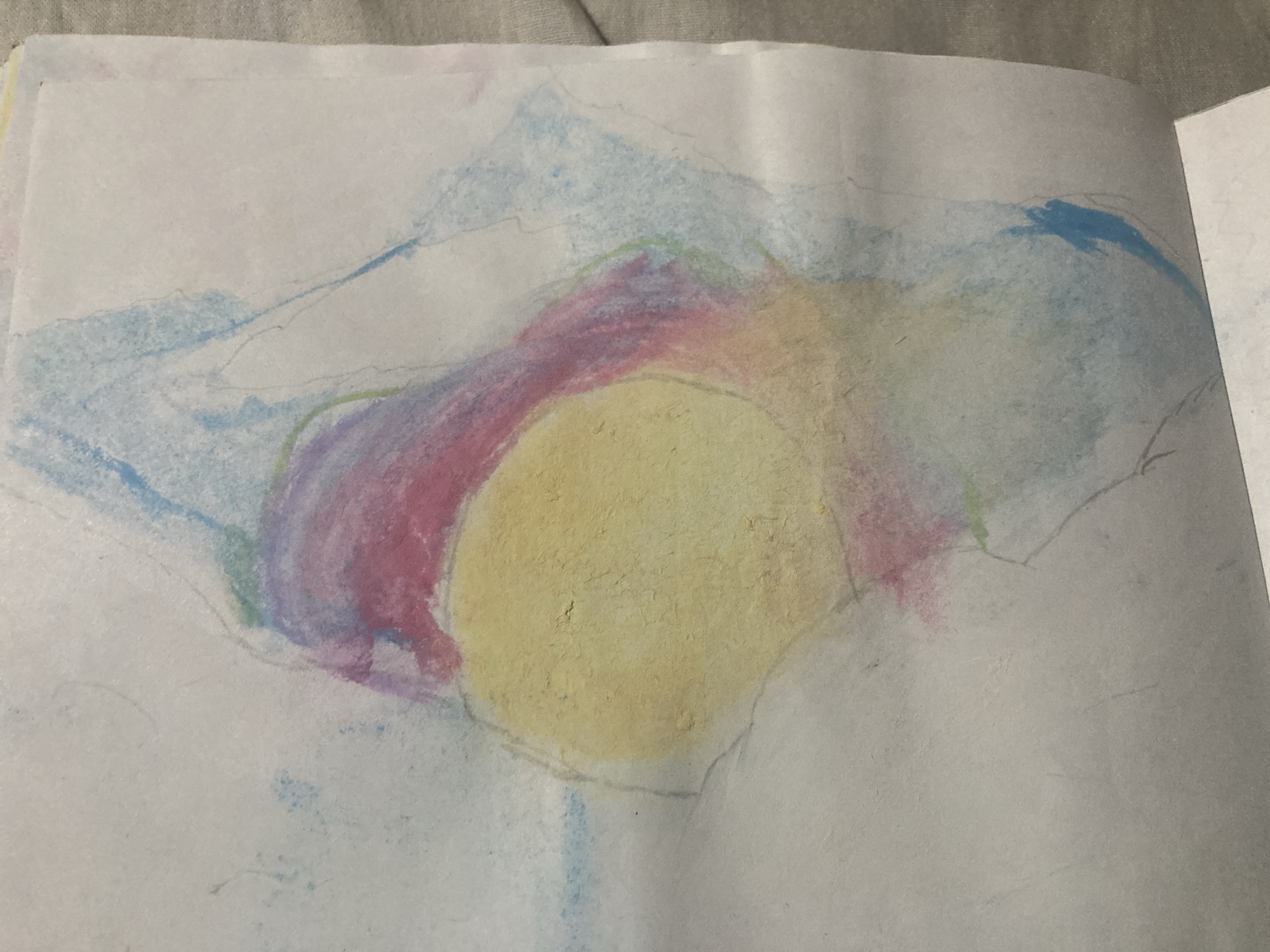 A colored pencil drawing on white paper depicts abstract shapes and colors. A central, irregular circular form is rendered in yellow and is surrounded by washes of pink, purple, and green. Lighter blue strokes appear in the upper left and right portions of the drawing, suggesting a sky or clouds. Thin, faint gray lines crisscross the entire image, possibly outlines or initial sketch marks. The drawing is slightly crumpled and appears to be a page from a sketchbook, as indicated by the visible right edge which shows a faint crease and the beginning of another page. There are no people, animals, or identifiable objects within the drawing. The drawing is presented on a gray, textured surface, likely a bedspread or blanket. The specific location of Besedy, Russia, is not depicted or suggested by the image content.