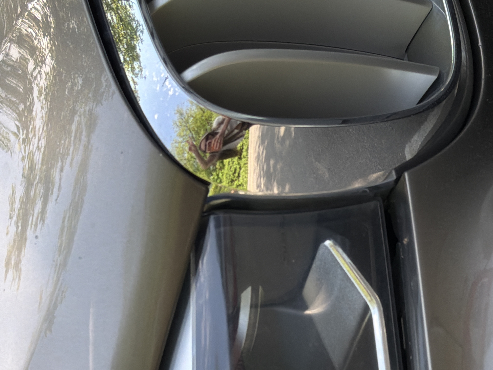 This close-up photo depicts the side of a light-colored vehicle, possibly a car, with a chrome-trimmed air vent visible. The reflection in the chrome shows a person standing outside, surrounded by trees, suggesting an outdoor setting. The vehicle's paint appears slightly weathered, and the overall scene implies an exterior shot taken during daylight. There is no indication in the photo that it is from Moscow, Russia.