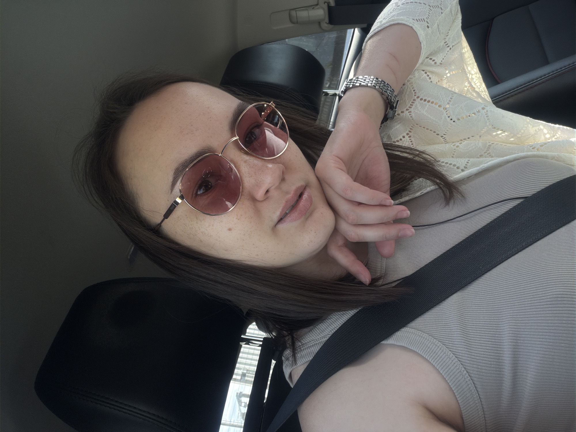 A woman wearing sunglasses and a seatbelt is sitting in a car. The environment is consistent with the inside of a vehicle, featuring a black headrest and a portion of the car's interior. The location in the city of Chaikovsky, Russia is not discernible from the image.