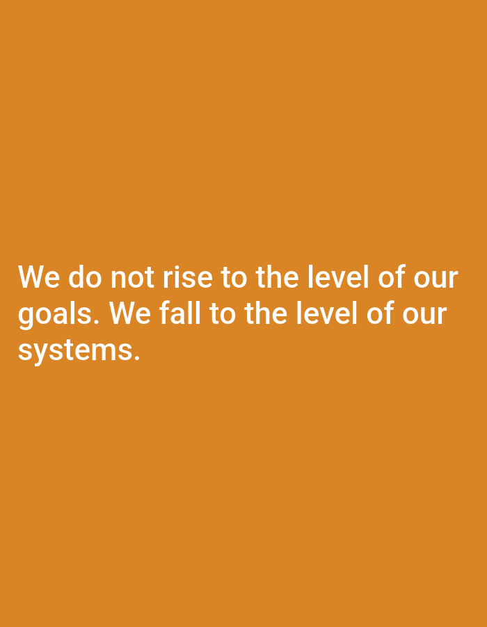 The image displays a white text overlay on an orange background. The text reads: "We do not rise to the level of our goals. We fall to the level of our systems." There are no people, objects, actions, interactions, or environmental details visible in the image, as it is a plain background with text. The location in Keffi, Nigeria, is not depicted or suggested by the image content.