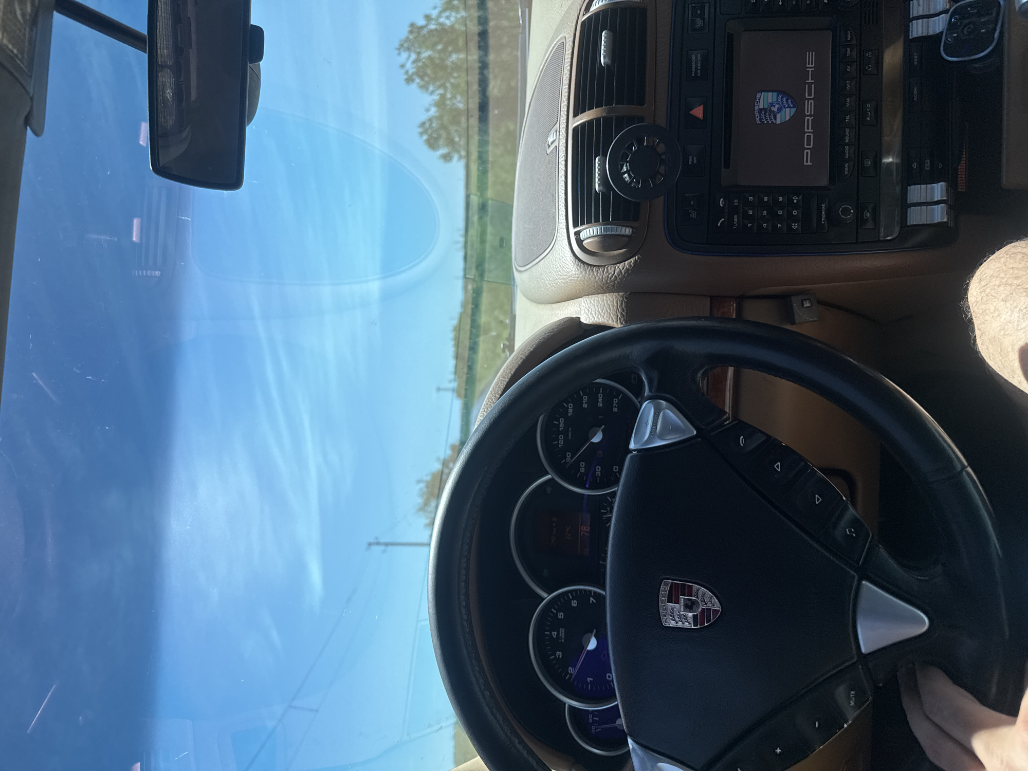 A view from inside a Porsche car, with the dashboard, steering wheel, and windshield visible. The car is parked, displaying the Porsche logo on the center console and steering wheel. The outside environment is blurred through the windshield. There are no clear indicators of the location being Glodjevo, Bulgaria. The picture doesn't show any people or interactions.