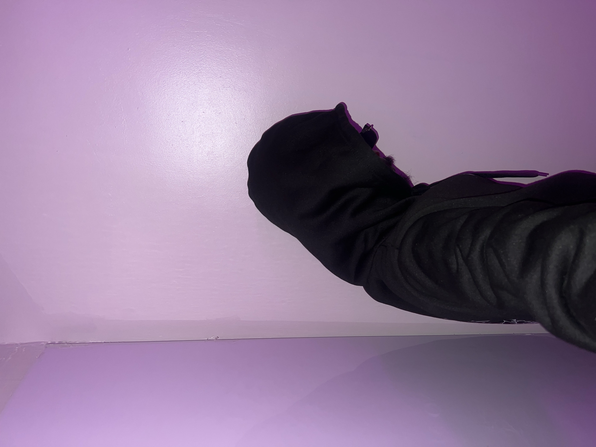 A person wearing a black hoodie is positioned at an angle against a light purple wall in a room. The hood is up, obscuring their face. The image provides no information regarding the location in Lagos, Nigeria.