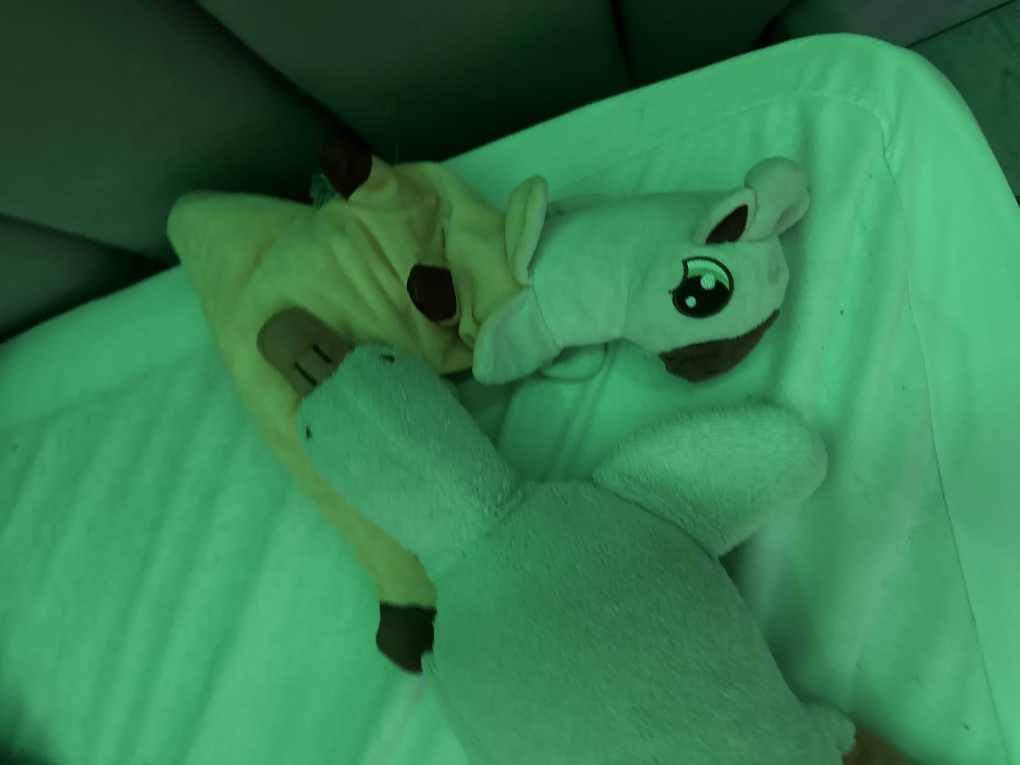 The image shows three stuffed animals lying on a light green surface, possibly a bed. One is a yellow and brown giraffe, another is a white horse, and the third is a white, unidentifiable animal, possibly a bird. The location is not specified, and there is no indication that the image was taken in Unknown, Russia. There are no people visible in the image.