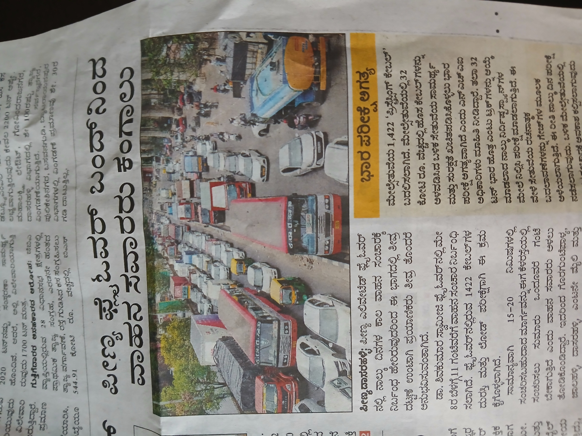 The image is a newspaper clipping, possibly from a Kannada language newspaper, featuring a photograph of heavy traffic on a road in Bengaluru, India. The traffic appears congested with cars, buses, and other vehicles. Overhead, there are structures resembling overpasses or elevated roadways. The accompanying text in Kannada discusses a temporary closure of the Peenya flyover for maintenance, causing traffic disruptions. The article mentions the need to replace prestressing cables and conduct load testing on the structure. Other details include the impact on commute times and alternative routes affected by the closure, like Goraguntepalya, Jalahalli, Dasarahalli, and 8th Mile.