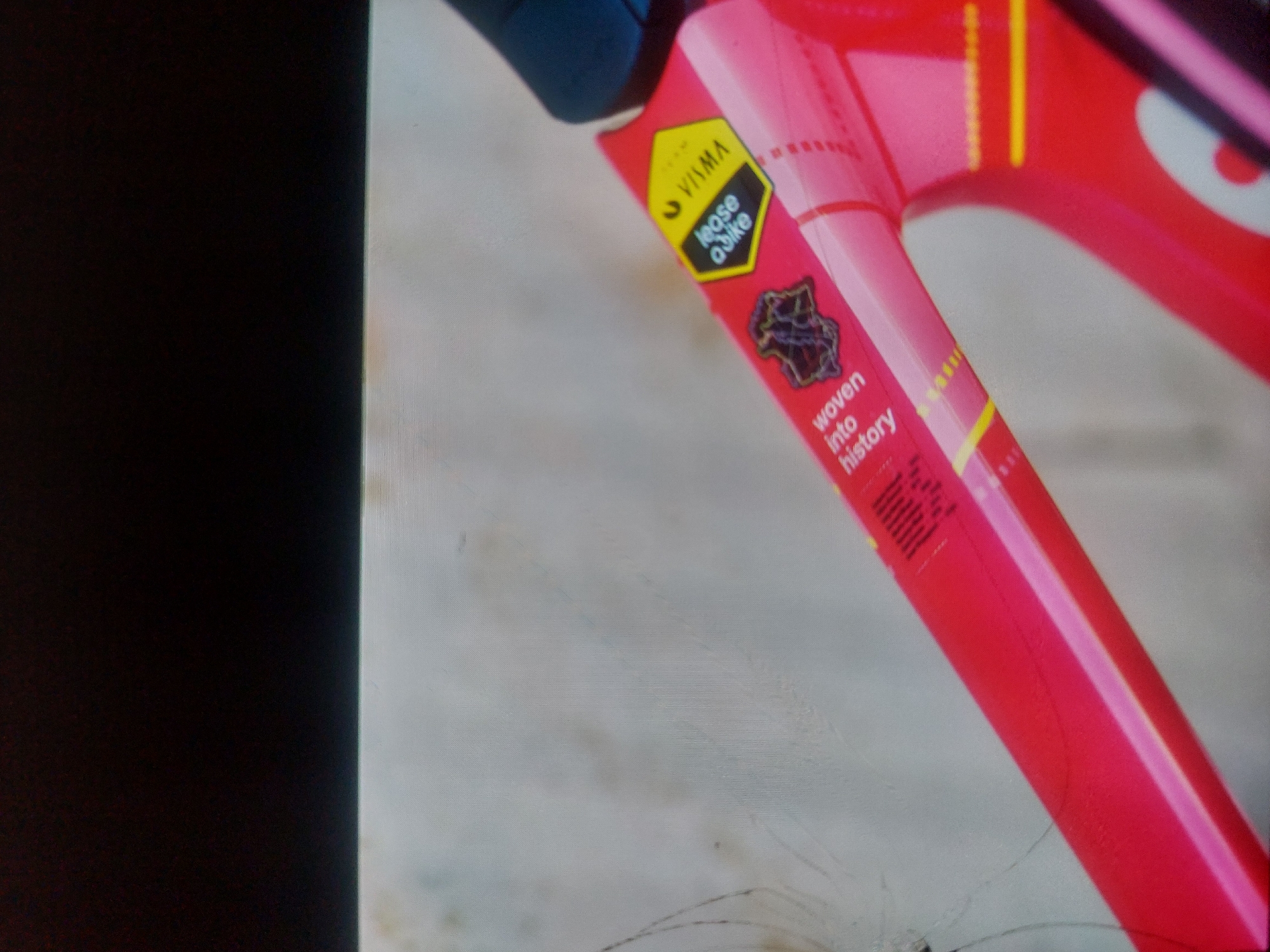 The image shows a close-up of a section of a red bicycle frame. On the frame, there is a yellow sticker with the brand "YAMA" and the words "lease a bike." Below that is a graphic and the text "woven into history." The photograph is taken indoors. It is impossible to determine the location in the city of Tsarevo, Bulgaria without additional information.