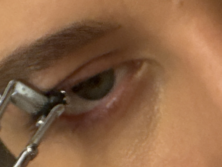 A close-up forensic image, taken in Vysokinichi, Russia, depicts the upper portion of a human face. The central subject is an eye, showing a dark iris and pupil, with the upper eyelid and a portion of the lower eyelid visible. A dark brown, well-groomed eyebrow arches above the eye. A metallic implement, silver in color, is positioned at the upper lash line, appearing to clamp or apply pressure to the eyelashes. The skin around the eye is of a medium-light complexion. No other persons or specific environmental elements are identifiable.