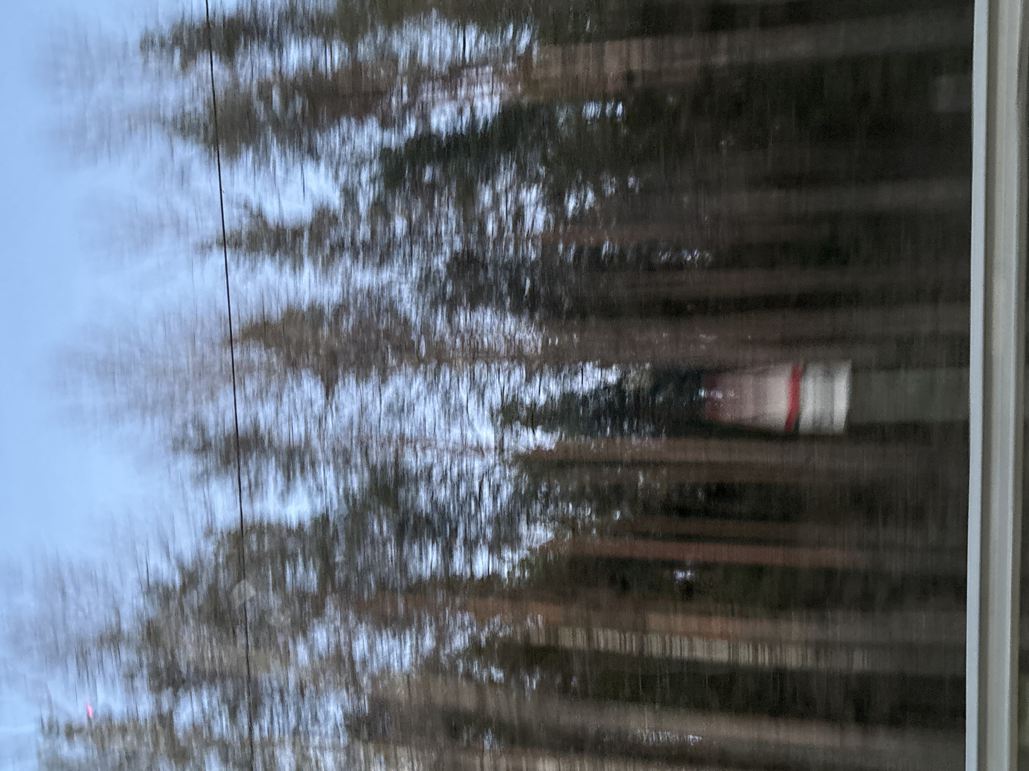 The image shows a view from a window, likely from a moving vehicle, perhaps a train, with blurred scenery including trees and what appears to be a building or train car passing by. The location is likely Yoksolovo, Russia. The blurry nature of the image indicates movement. There's a wire visible in the upper left area. The right side of the image reveals the edge of the window frame.