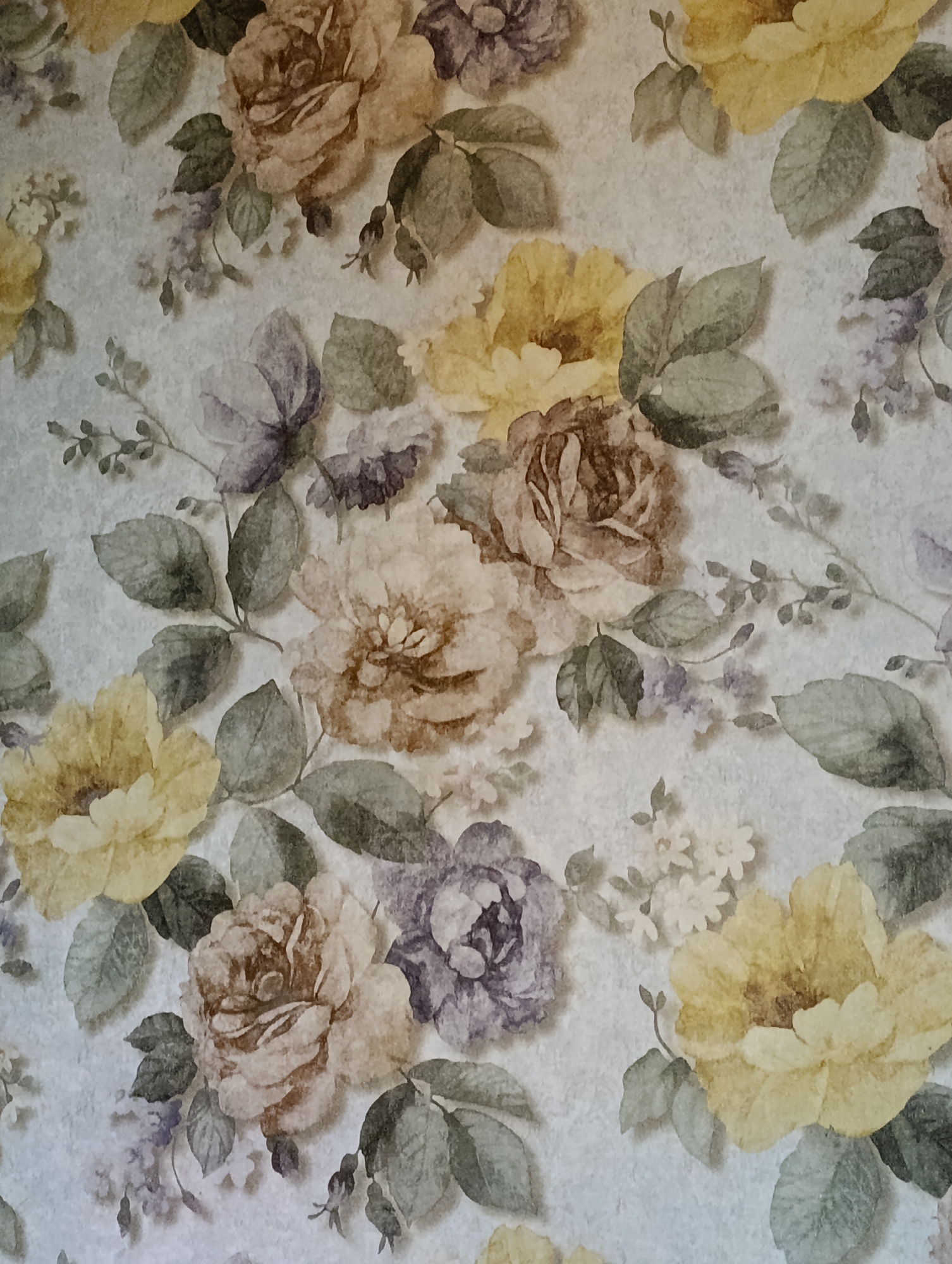 The image shows a close-up view of floral wallpaper. The wallpaper features a pattern of roses and other flowers in muted shades of yellow, brown, and purple, with green leaves. The background is a textured, light gray. There are no people, actions, or interactions visible in the image. The specific location in Halkabad, Uzbekistan, is not discernible from the image itself, as it is a pattern on wallpaper.
