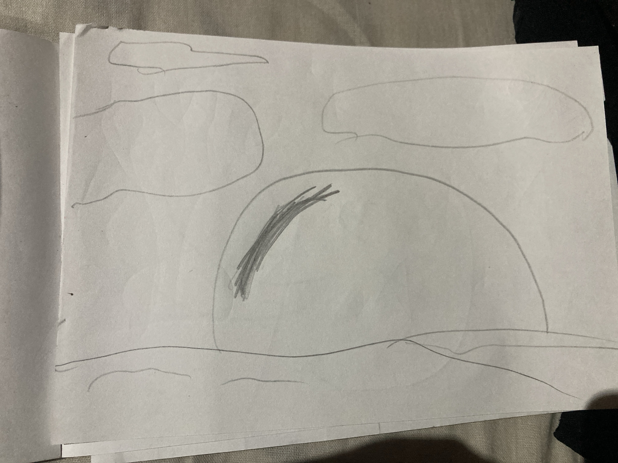 The image shows a close-up of a piece of paper with a simple pencil drawing on it. The drawing appears to be abstract or figurative, with several curved lines and shaded areas. There are no discernible landmarks or clues within the drawing itself that would indicate a specific location in Besedy, Russia. The background of the image is a textured surface, possibly a bed or sofa, which is out of focus. The paper itself is slightly wrinkled and appears to be part of a sketchbook or notepad.