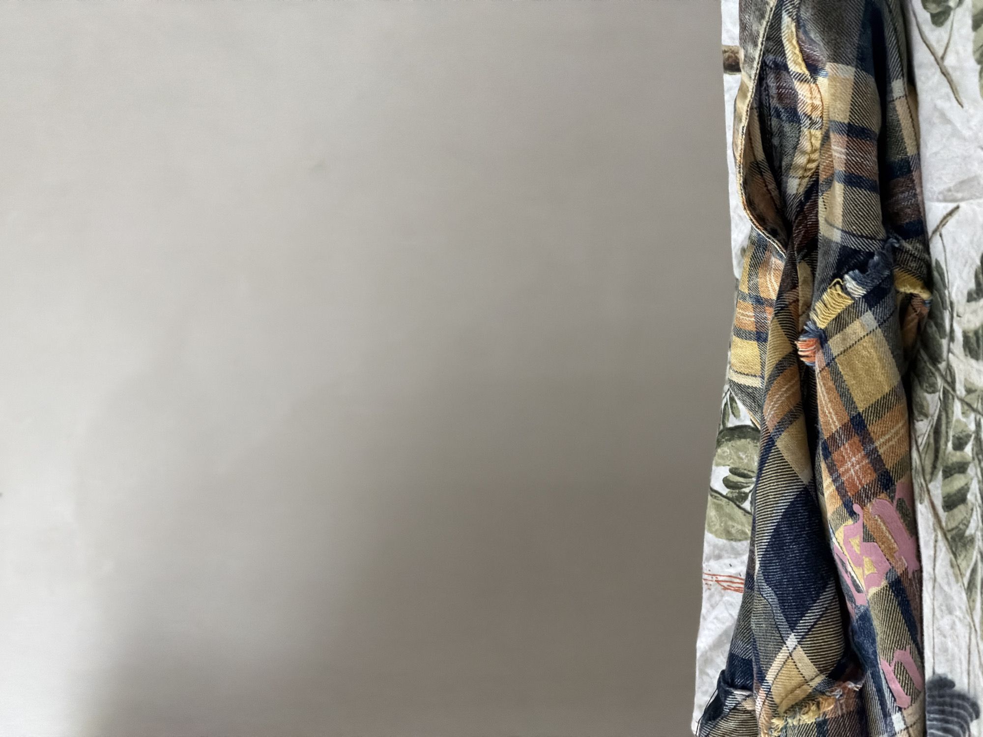 The image shows a gray wall on the left and some clothing items on the right. The clothing appears to include a plaid shirt in shades of tan, blue, and brown, and a white patterned garment with green foliage designs.
The image does not contain any information to identify the location as the city of Strelna, Russia.