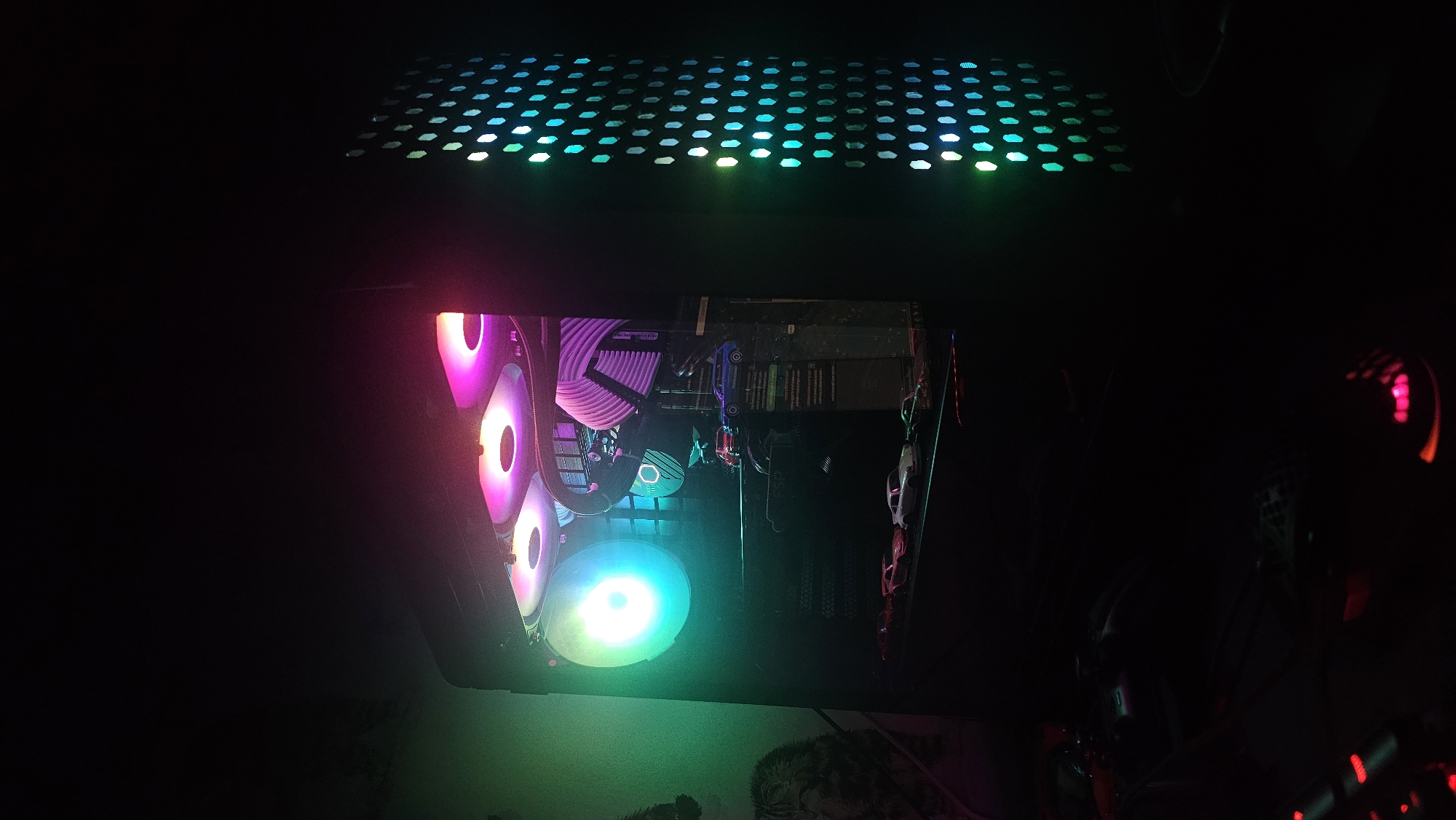The image shows the interior of a computer case with various components illuminated by RGB lighting. Visible components include cooling fans, a motherboard, RAM modules, and a power supply. The top of the case has a perforated grill with illuminated RGB elements. Due to the lack of external visual references, it is impossible to determine the location in Varna, Bulgaria.