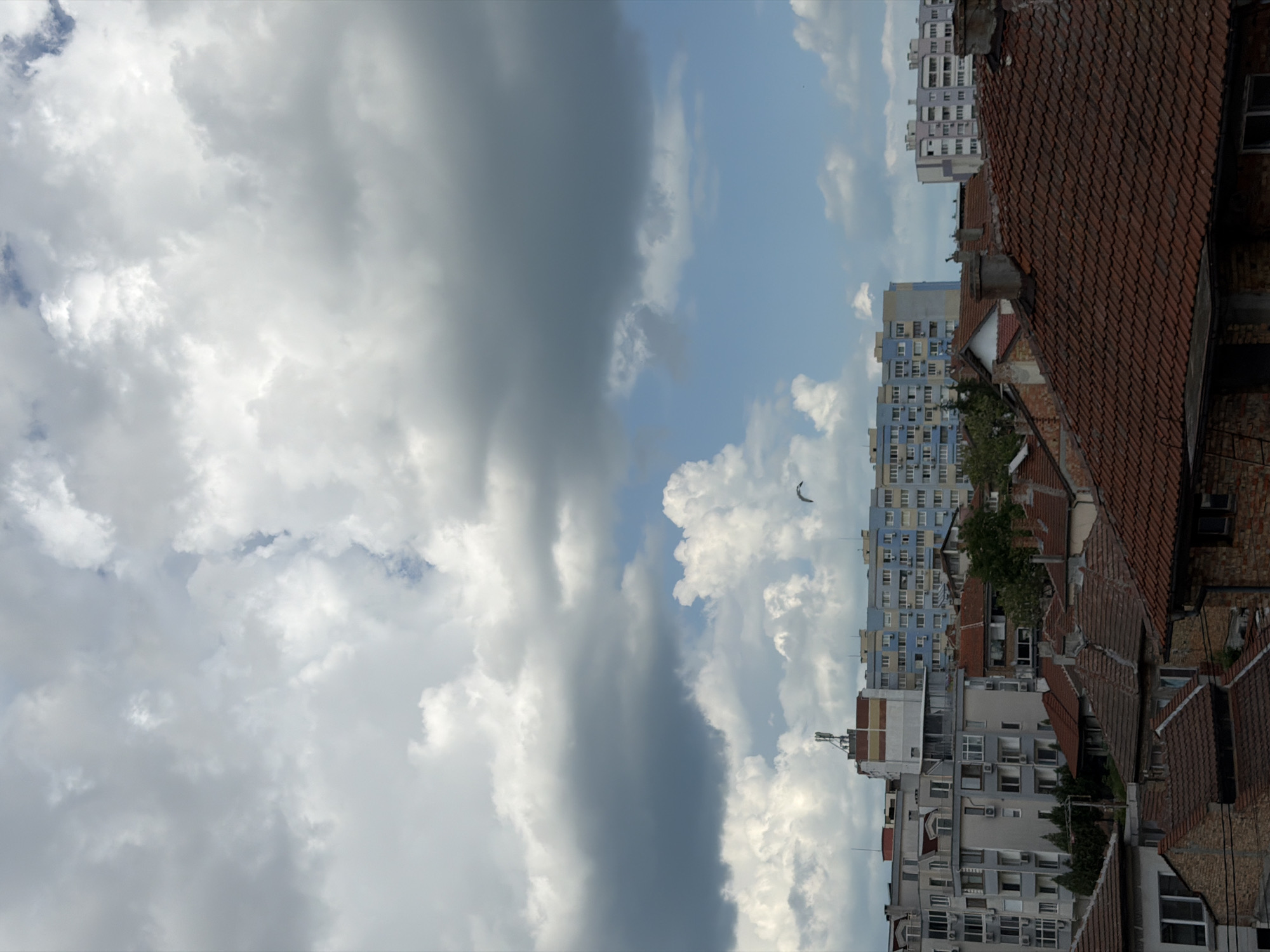 View of buildings and clouds, possibly in Burgas, Bulgaria. Tile roofs and apartment buildings are visible. Heavy clouds occupy the left side of the frame.