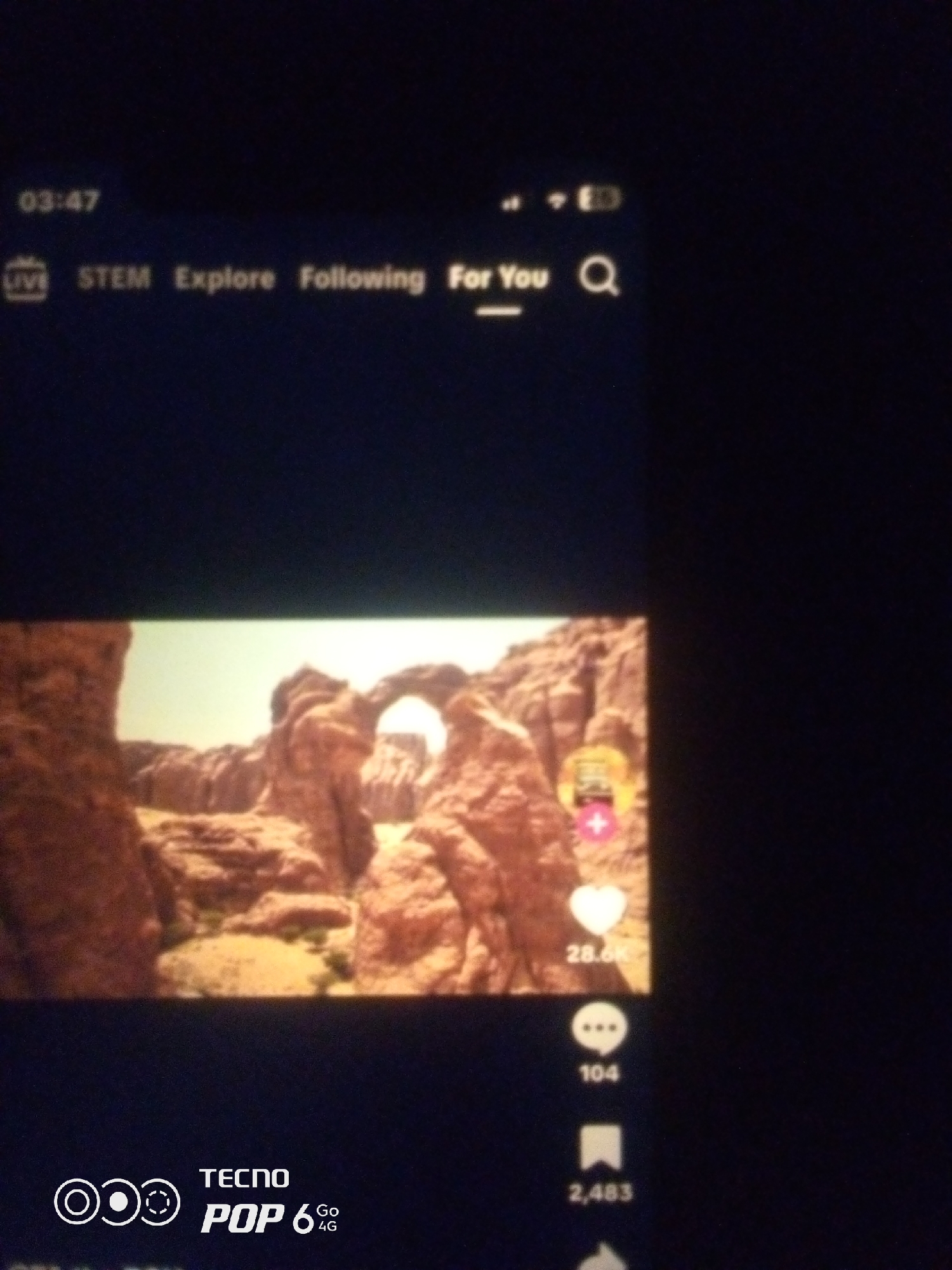 The image displays a smartphone screen showcasing a TikTok-like interface. At the top, the time "03:47" is visible, followed by navigation options: "LIVE", "STEM", "Explore", "Following", and "For You". A search icon is also present. The main content of the screen is a video featuring a natural landscape with rock formations and an arch. On the right side of the video, interactive elements are displayed: a heart icon with "28.6K" indicating likes, a speech bubble icon with "104" for comments, and a bookmark icon with "2,483" for shares or saves. At the bottom of the screen, a Tecno Pop 6 4G logo is visible. There are no identifiable people or specific locations within the city of Howayi, Nigeria, depicted in this image.
