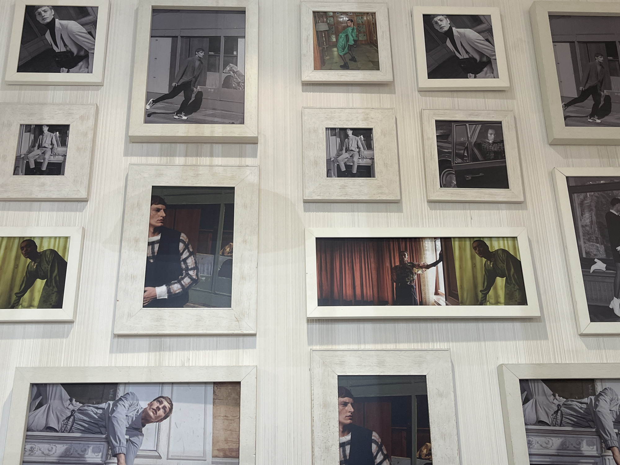 The image displays a collection of framed photographs arranged on a white vertically striped wall, likely an interior setting. The photographs are predominantly in black and white, with some in color. They depict various individuals in what appear to be fashion or portrait-style scenes, suggesting a photography studio or a fashion-related establishment. No specific details confirm the location as Saint Petersburg, Russia, without additional visual or contextual clues.