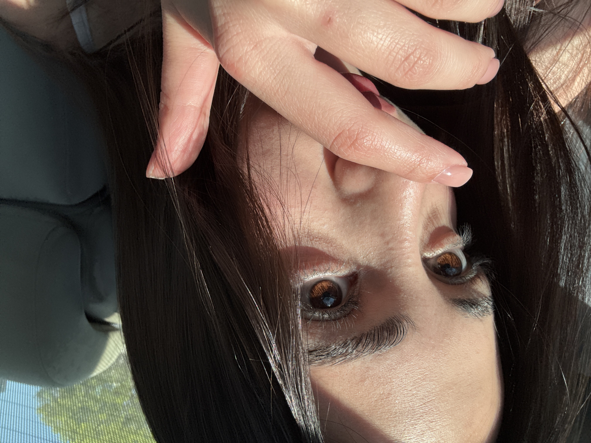 The image shows a close-up of a person's face with brown eyes, dark hair, and light skin. The person's hand is positioned near their forehead. The location appears to be indoors with light shining in. There is no verifiable information to indicate this photo was taken in Yerevan, Armenia.