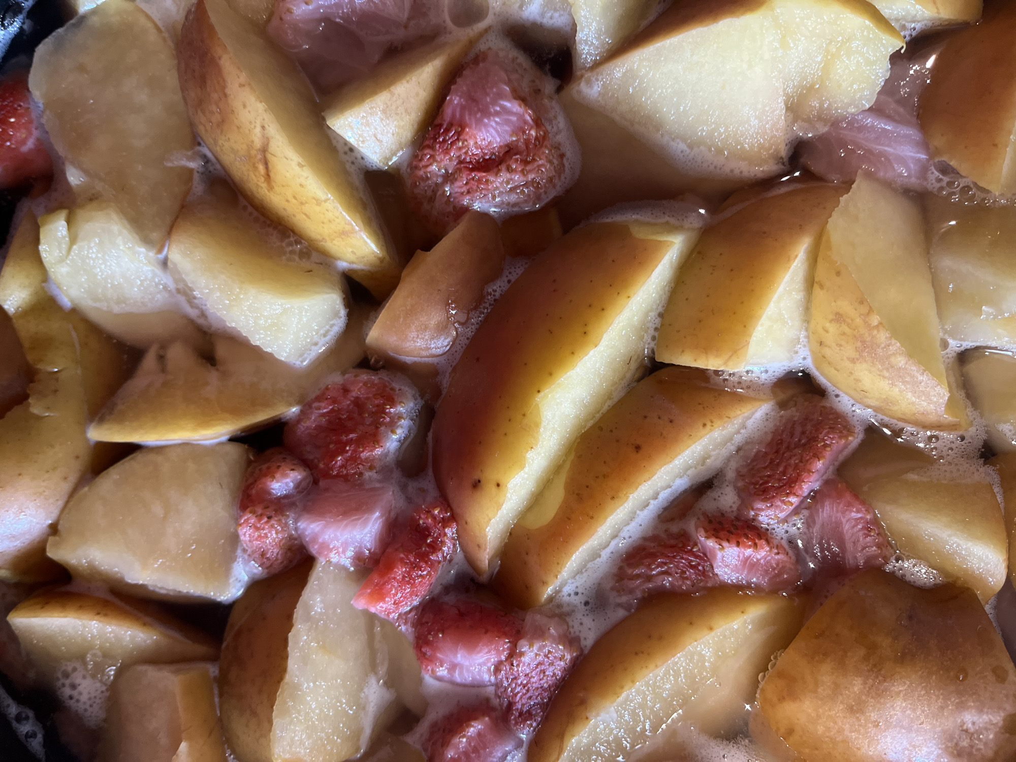 The image shows a close-up, overhead view of chopped strawberries and what appear to be sliced pears simmering in a liquid. The fruit pieces are varied in size and shape, with the strawberries exhibiting their characteristic red color and texture, while the pear slices are light yellow and golden brown. The liquid is frothy and appears to be bubbling, suggesting it is being heated. There is no identifiable location in Warsaw, Poland visible in this image; it is a simple food preparation scene.