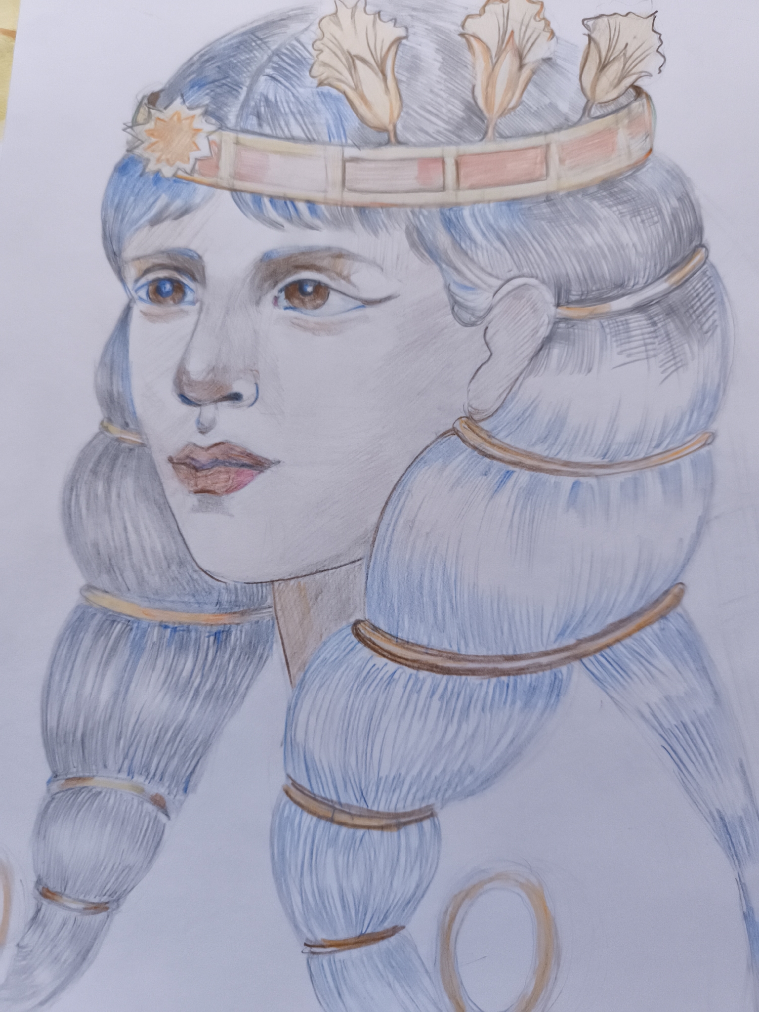 The image is a close-up, colored pencil drawing of a person's head and shoulders. The subject has blue hair styled in two large braids, each adorned with gold bands. They wear a golden crown embellished with what appear to be stylized petals or leaves. The crown also features a star-shaped ornament on the front. The person has brown eyes, a light complexion, and is looking to the left. The drawing is done on white paper. There is no discernible location within the city of Saint-Denis, France.