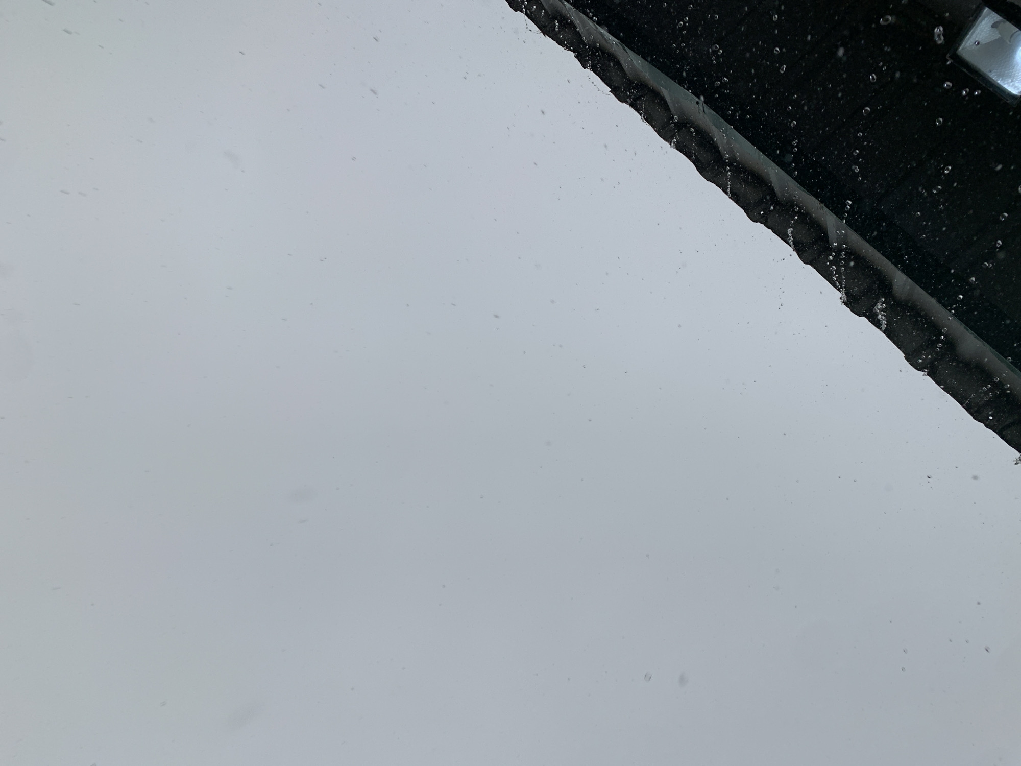 The image shows a gray sky with some light snowfall or rain. In the top right corner, a dark, possibly black structure is visible, with droplets of water on its surface. A light source is visible on the edge of the structure. The majority of the image is filled with the overcast sky, suggesting an outdoor setting. The location and specific details are not discernible from the provided image. New Stadium, Nigeria is irrelevant.