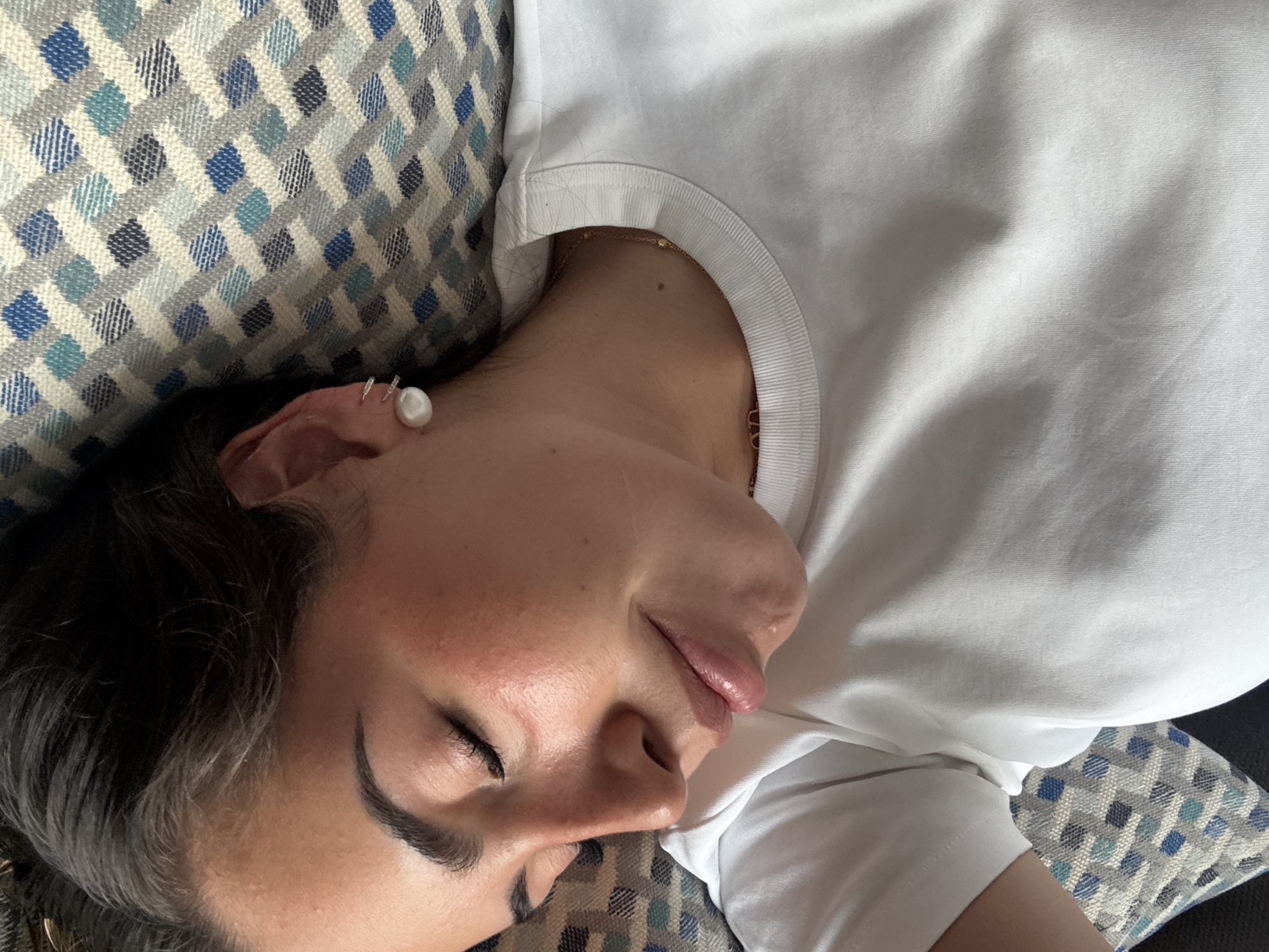 A person is lying down on a patterned pillow, wearing a white shirt. The person appears to be sleeping. The pillow has a geometric pattern in shades of blue, grey, and white. The location of the image is unknown and there is no information about the city of San Bernardino Tlaxcalancingo, Mexico.