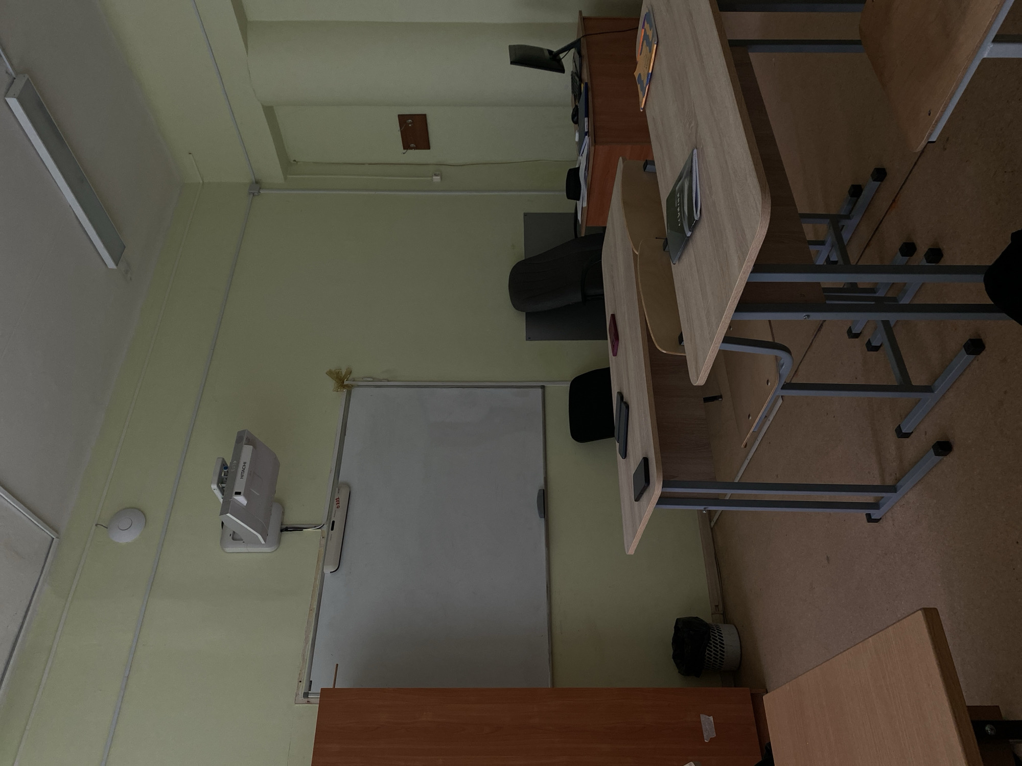 The image shows an empty classroom in Kazan, Russia. The classroom is furnished with student desks and chairs, a teacher's desk, a whiteboard, and a projector mounted on the wall. The classroom appears to be unoccupied.