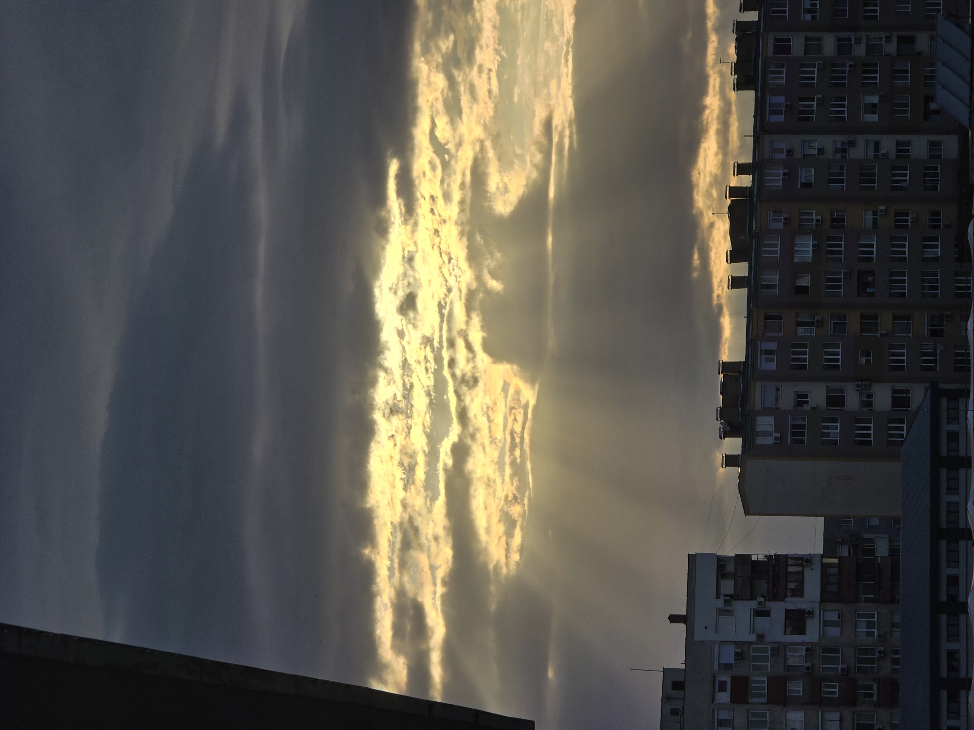 The image shows a sky with clouds illuminated by the sun and a building. The location of the city is unknown. The building is a large, multi-story structure.