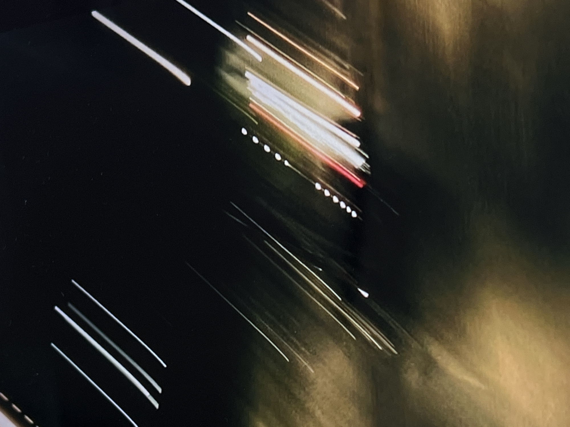 The image captures a blurred, abstract scene of light trails, likely from vehicle headlights and taillights at night. The dark background suggests an outdoor urban environment. The light trails are elongated and diagonal, indicating movement. There are streaks of white, red, and yellow light, consistent with car lights. The lower portion of the image shows a yellowish, diffused light, which could be streetlights or reflections on a wet surface. The overall impression is one of motion blur in a city setting. There is no discernible detail to indicate the specific location in Genemuiden, Netherlands.