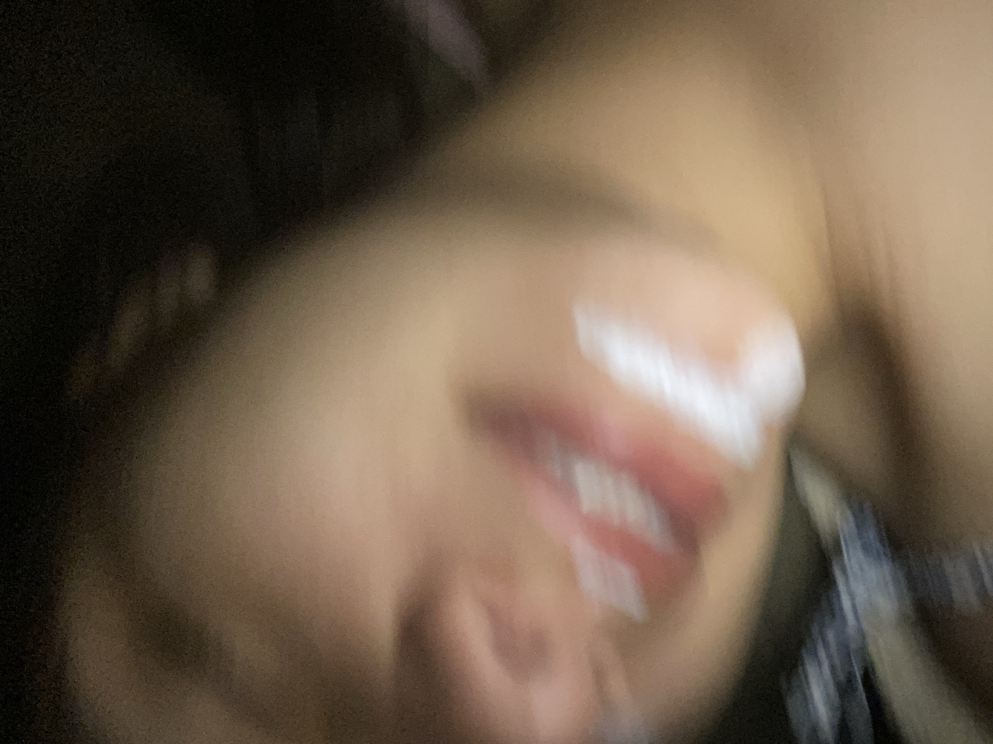 This extremely blurry, close-up image captures what appears to be a person's mouth and lower face, possibly angled upwards. The dominant features are the lips, which are partially obscured by a white, creamy substance, likely whipped cream or frosting, suggesting an act of eating or playful application. The skin around the mouth is visible, indicating a light to medium complexion. The extreme motion blur makes it impossible to discern clear facial features, expression, or the exact details of the substance.
The background is dark and completely out of focus, offering no specific environmental cues or objects. This lack of detail makes it difficult to determine the time of day, weather, or specific location within Cotoperíz, Venezuela. The blurriness could be due to fast movement of the subject, camera shake, or low light conditions. No text is visible in the image. The overall impression is one of an intimate, candid moment, possibly playful, but its interpretation is limited by the profound lack of clarity.