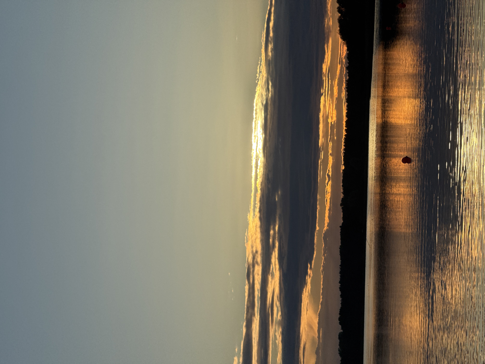 The image depicts a serene sunset over a body of water, likely a lake or a bay. The sky is a gradient of soft blues and yellows, transitioning into vibrant oranges and reds as the sun dips below the horizon. Wispy clouds are illuminated by the setting sun, creating a dramatic and colorful display.
In the foreground, the water is calm, with gentle ripples reflecting the colors of the sky. A dark silhouette of a treeline forms the horizon, suggesting a natural landscape. There are several small, red buoys floating on the water's surface, which might indicate a designated swimming area or a marker for a watercourse. The overall impression is one of peace and natural beauty.
While the image is beautiful, there are no specific landmarks or visual cues that would definitively place this scene in Tallinn, Estonia. The elements depicted are common to many coastal or lakeside areas, and without additional context, it is impossible to confirm its location within the city.