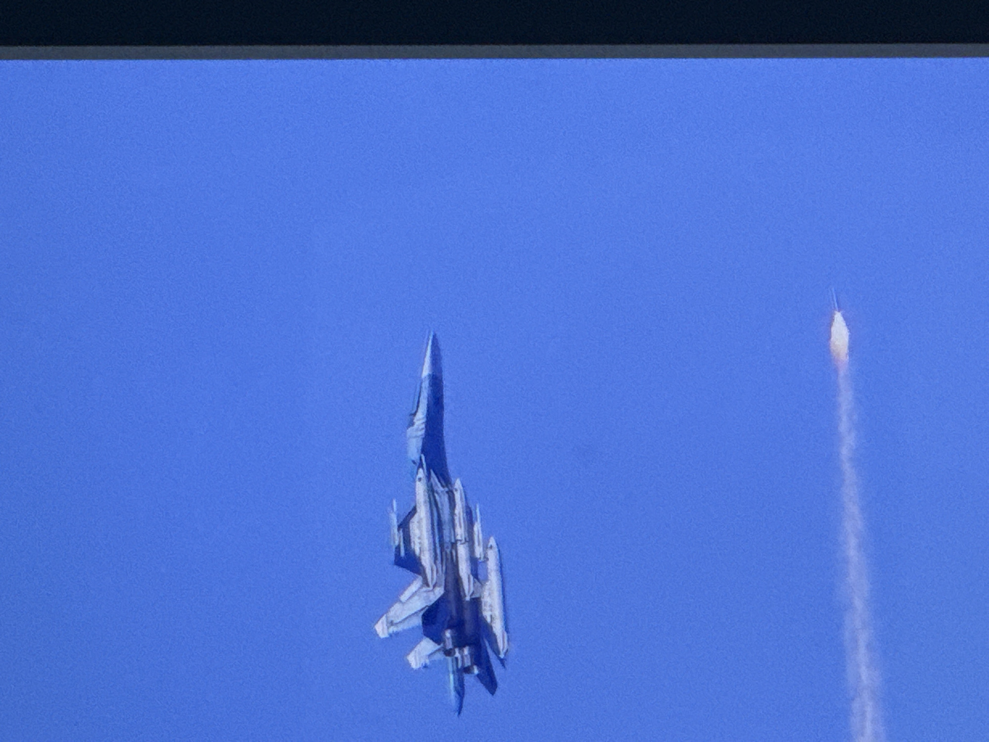 A fighter jet is captured in flight against a clear blue sky. Below the jet, a white contrail streaks across the sky, indicating its rapid movement. The jet appears to be equipped with multiple external pods or missiles. The scene is devoid of any urban or natural landmarks, making it impossible to determine a specific location within Cahul, Moldova, or any other city.