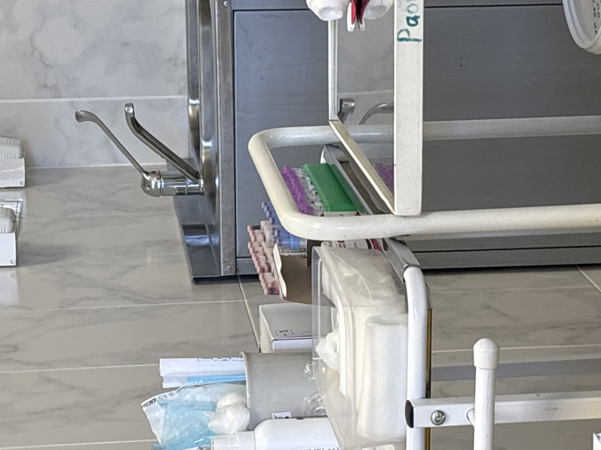 The image depicts a medical setting, possibly a clinic or hospital, featuring a sink with a lever-operated faucet. Adjacent to the sink is a medical cart laden with supplies, including test tubes, a container of wipes, a box, and various sterile medical products in packaging. The background consists of a smooth, tiled wall and floor, indicative of a sterile environment. The location in the city of Saint Petersburg, Russia is not discernible from the visual information provided.