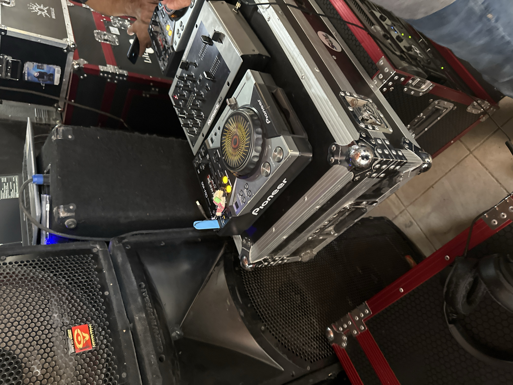 The image shows a DJ setup, likely indoors, consisting of a Pioneer CDJ-400 turntable, a Numark M2 mixer, and a Cerwin Vega speaker. The equipment appears to be housed in flight cases. A hand is visible near the top of the frame, possibly operating the mixer. The environment suggests a setting for music performance, such as a club or event venue. The location in the city of Puebla, Mexico is not evident from the image.