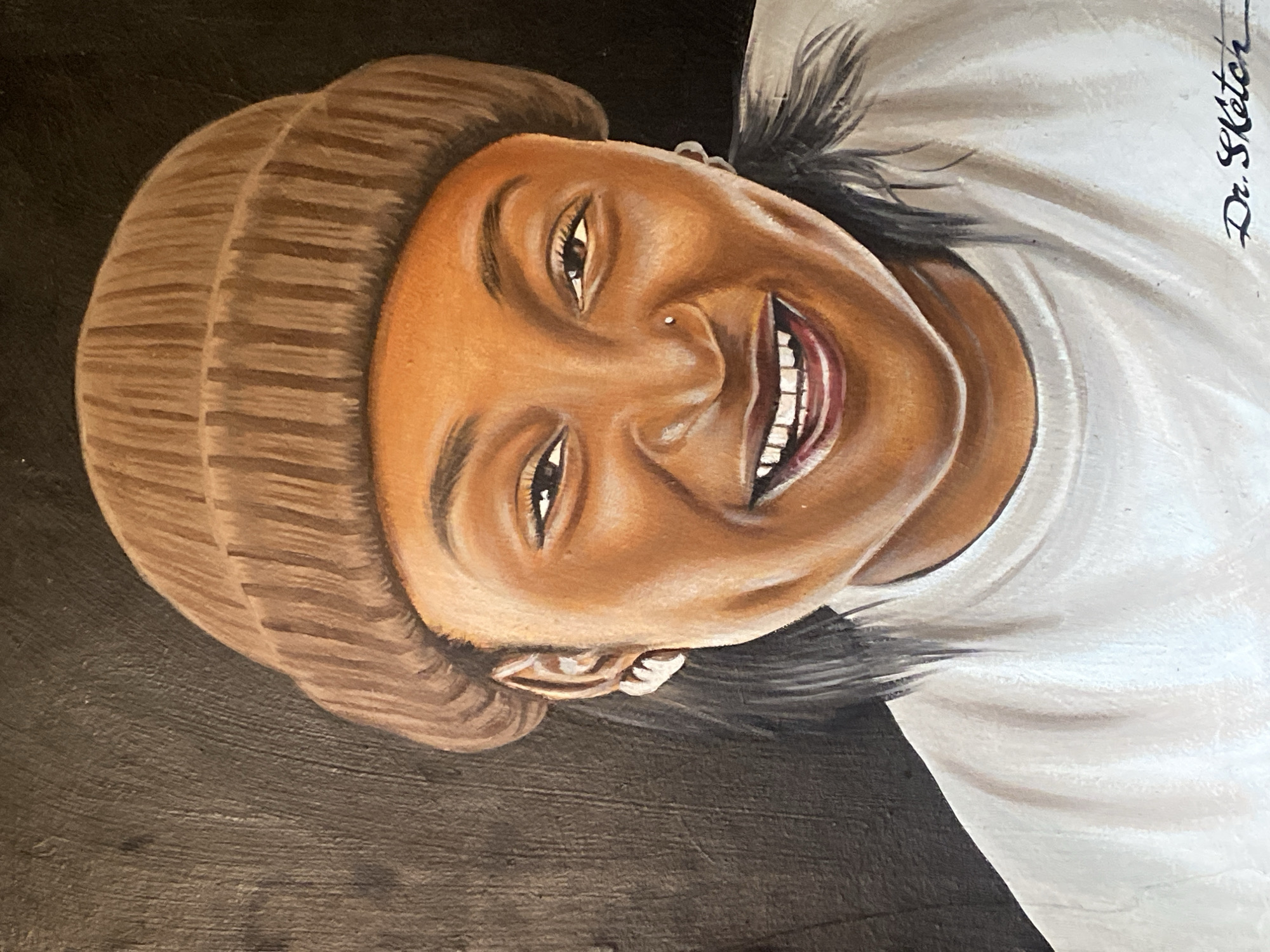 A portrait painting depicting a smiling woman with dark skin, wearing a brown knit hat and a white t-shirt. She has dark hair and a nose piercing. The background is dark brown. The signature "Dr. Sketch" is visible in the upper right corner of the image. The location, Barakin Akawo, Nigeria, is not evident in the image.