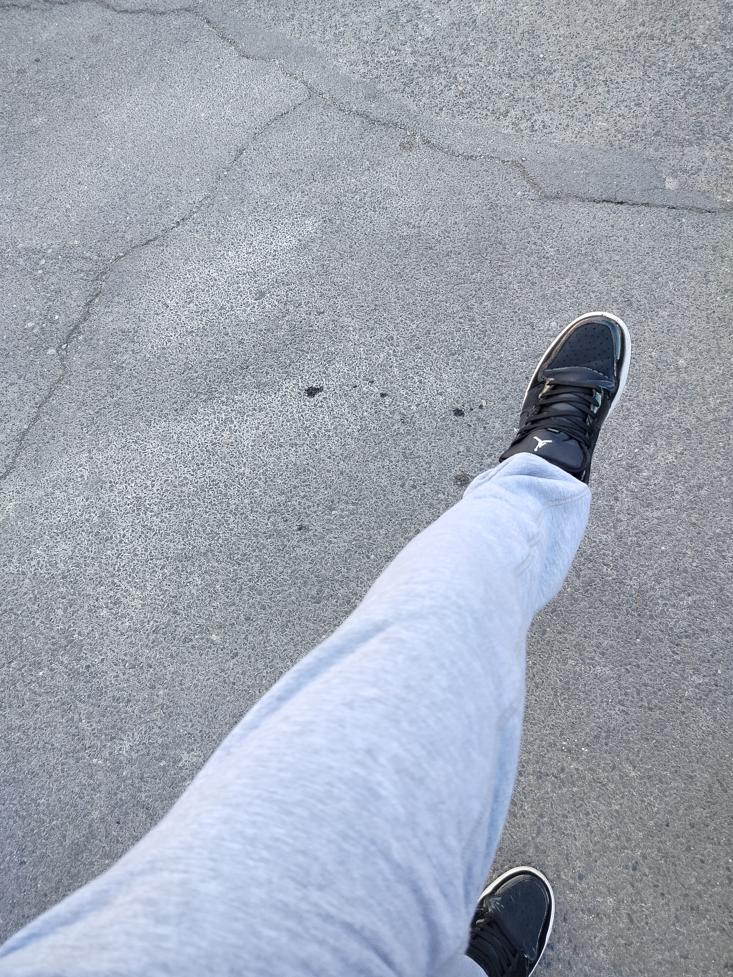 The image shows a first-person perspective view of a person standing on a concrete surface. The person is wearing light gray sweatpants and black and white Air Jordan sneakers. The concrete surface has cracks and a slightly rough texture. The location in the city of Yerevan, Armenia cannot be ascertained from the image.