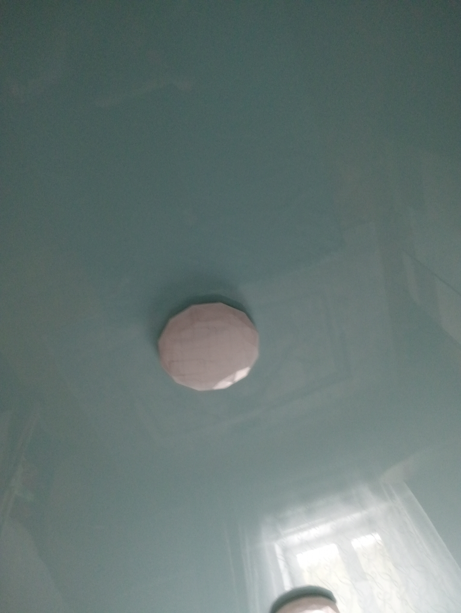 A light blue ceiling is visible in the image. In the center of the image, there is a round, white object that appears to be a smoke detector. In the lower right corner of the image, a window with sheer curtains is visible, and a person's head is partially visible in the bottom center of the image. The overall lighting is dim.
